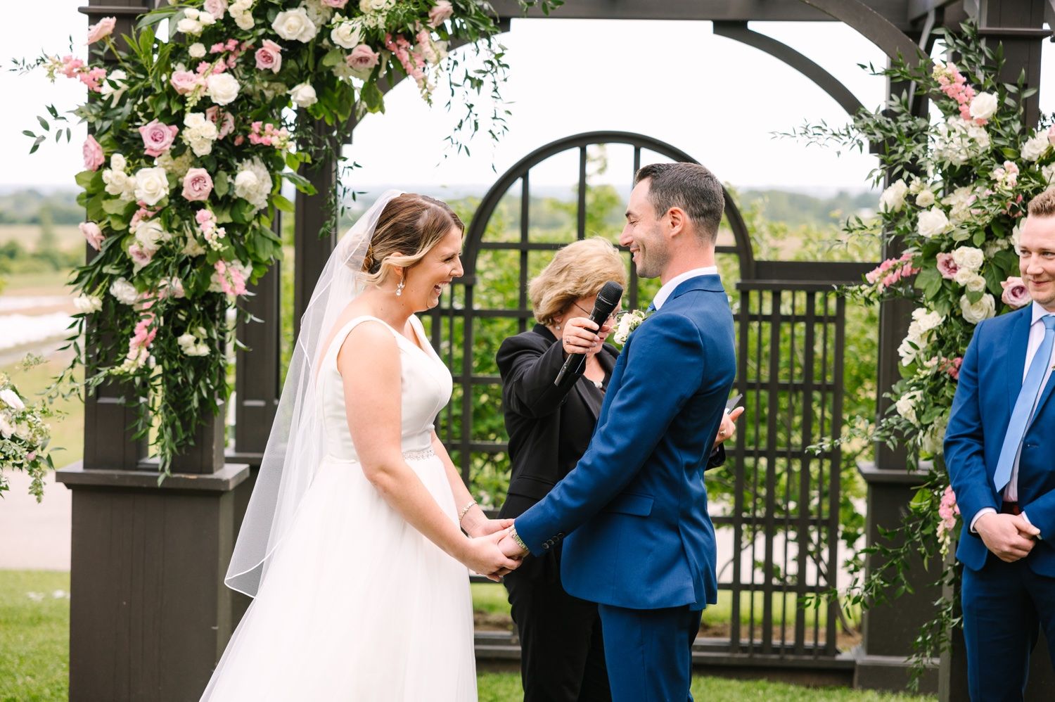 Wedding ceremony under floral arch with pink roses and greenery decorations.