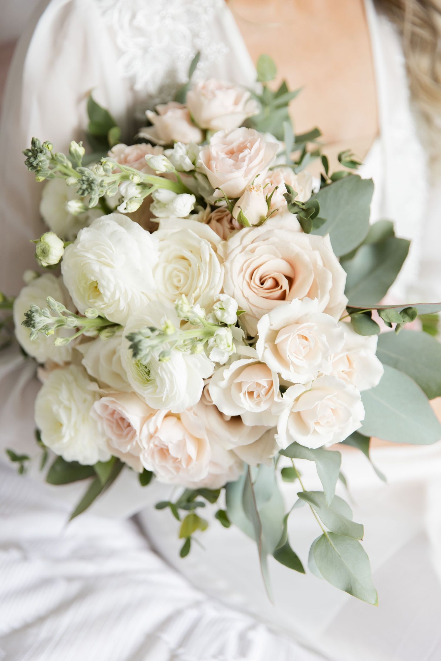 Soft and romantic bridal bouquet featuring blush roses, white ranunculus and eucalyptus leaves.