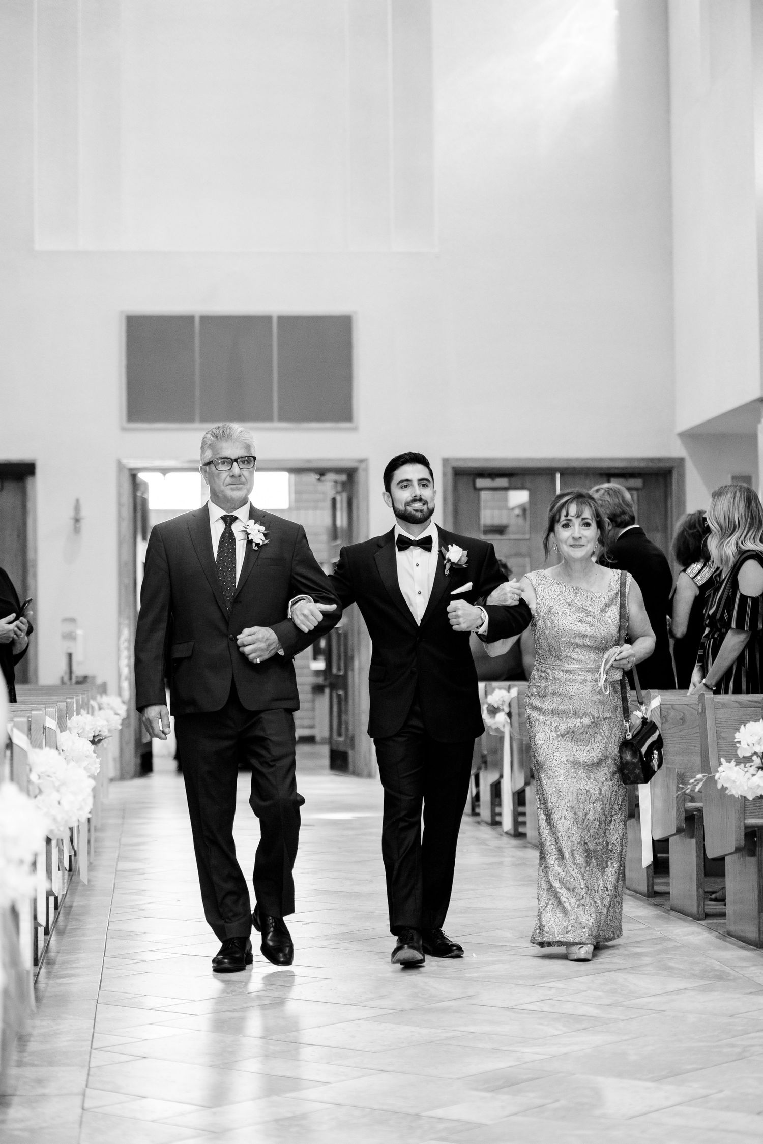 Wedding party members walking down the church aisle in formal attire.