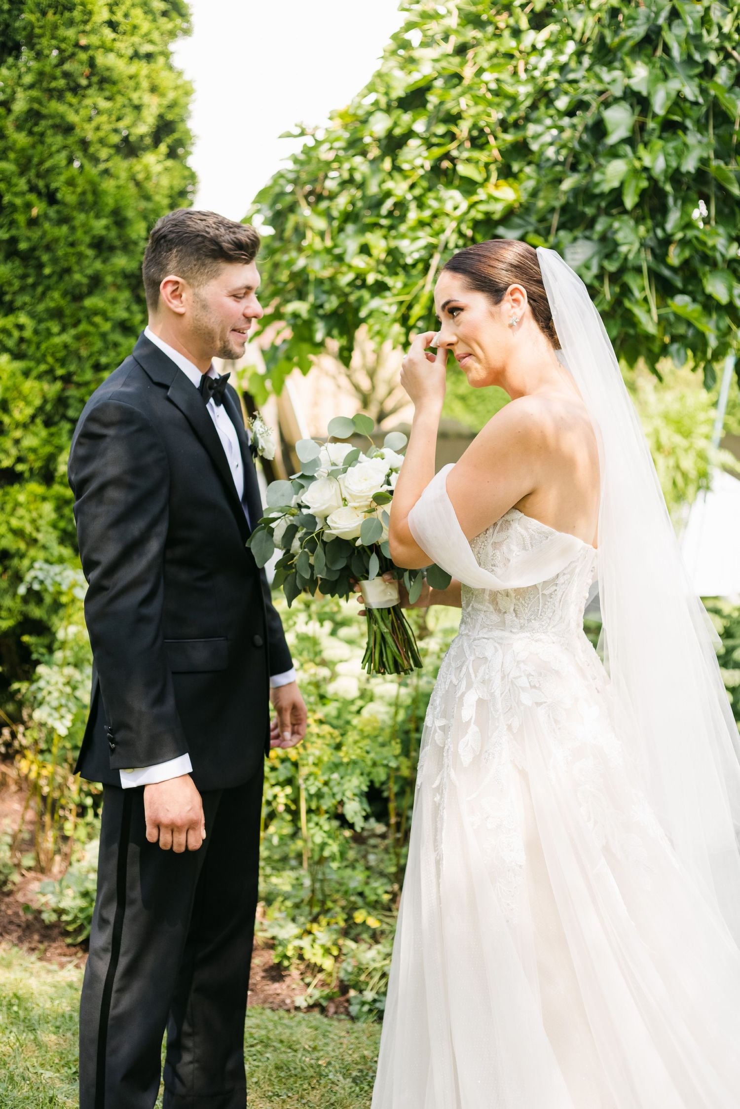 Candid outdoor wedding moment with couple sharing tears of joy in front of ivy-covered wall.