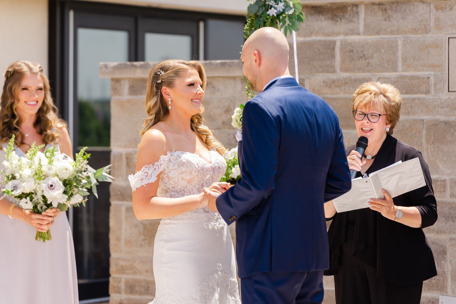 An emotional outdoor wedding ceremony moment with an officiant presiding over the exchange of vows.