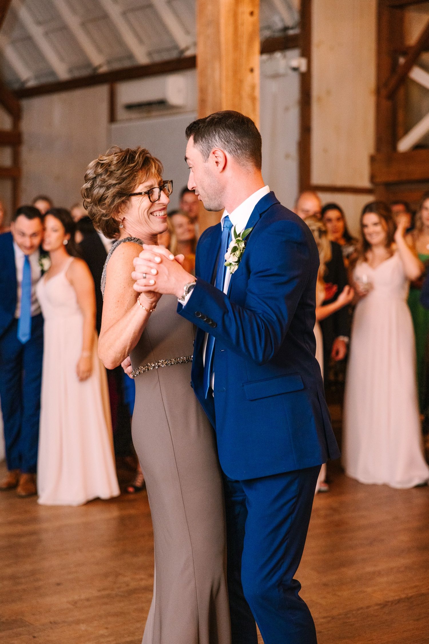 An elegant couple dancing in close embrace at a wedding reception with guests in the background.