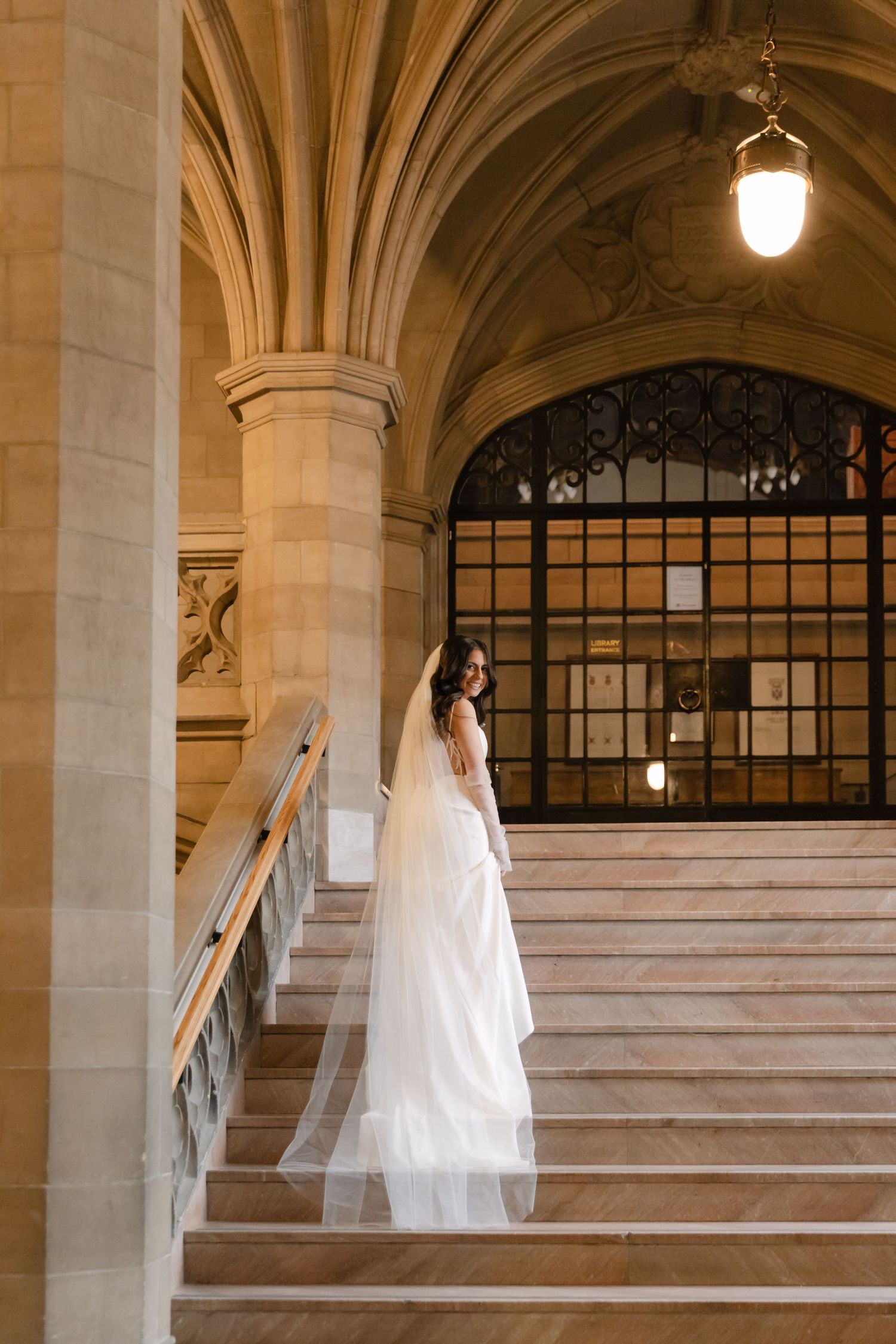 Elegant bridal portrait on stone steps with gothic architectural details and warm lighting.