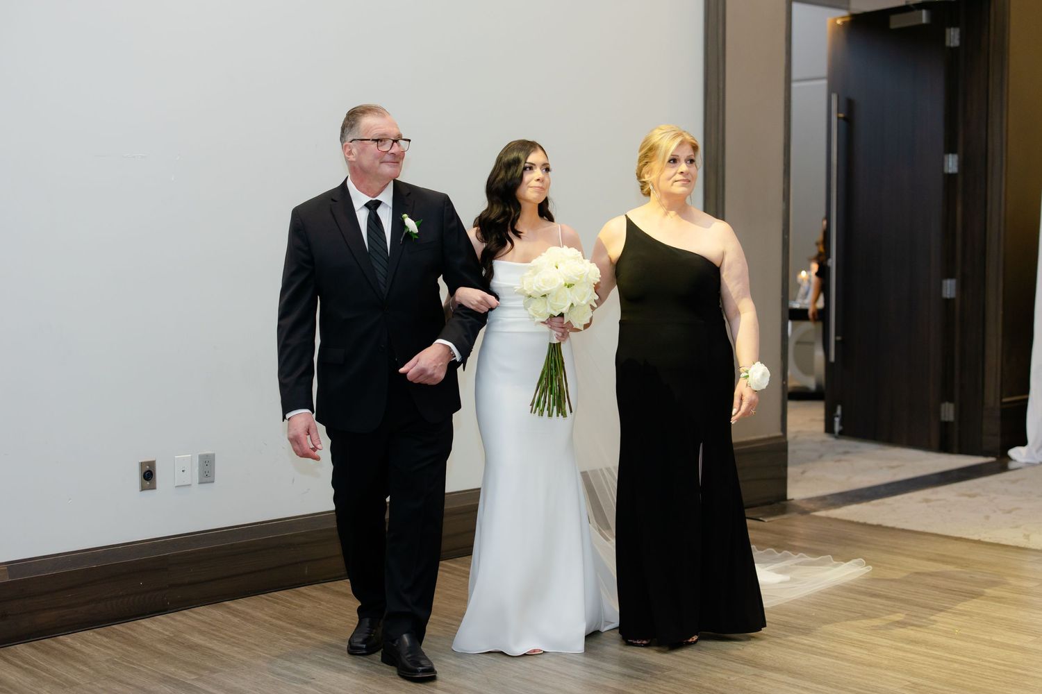 Wedding party members escort a bride in a classic white gown down the aisle.