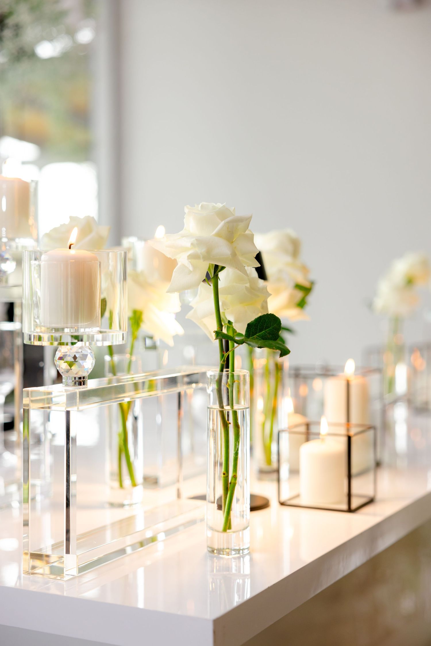 Modern wedding decor featuring white roses in crystal vases with glowing candles.