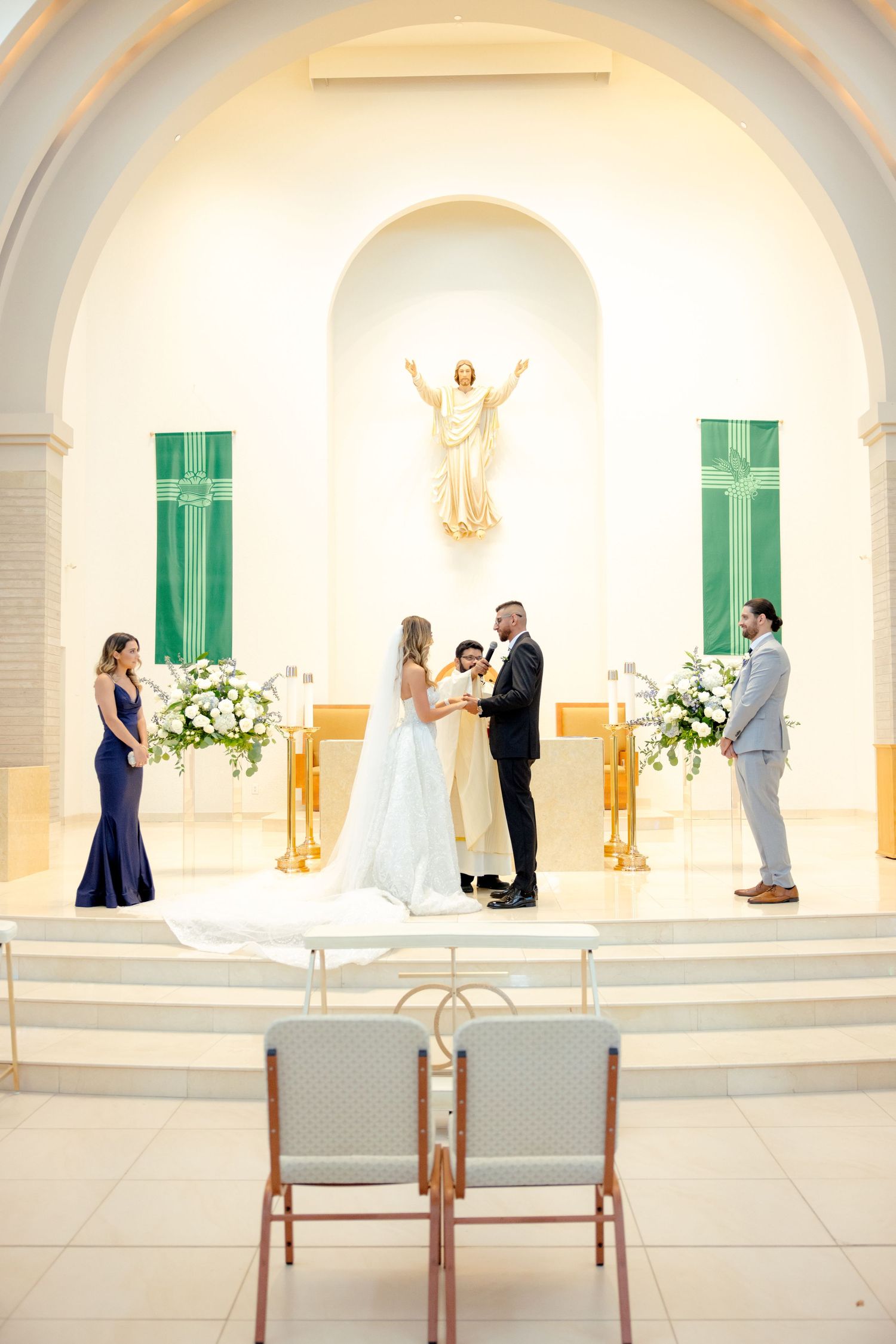 A wedding ceremony taking place at an altar with emerald green shutters and white floral arrangements.