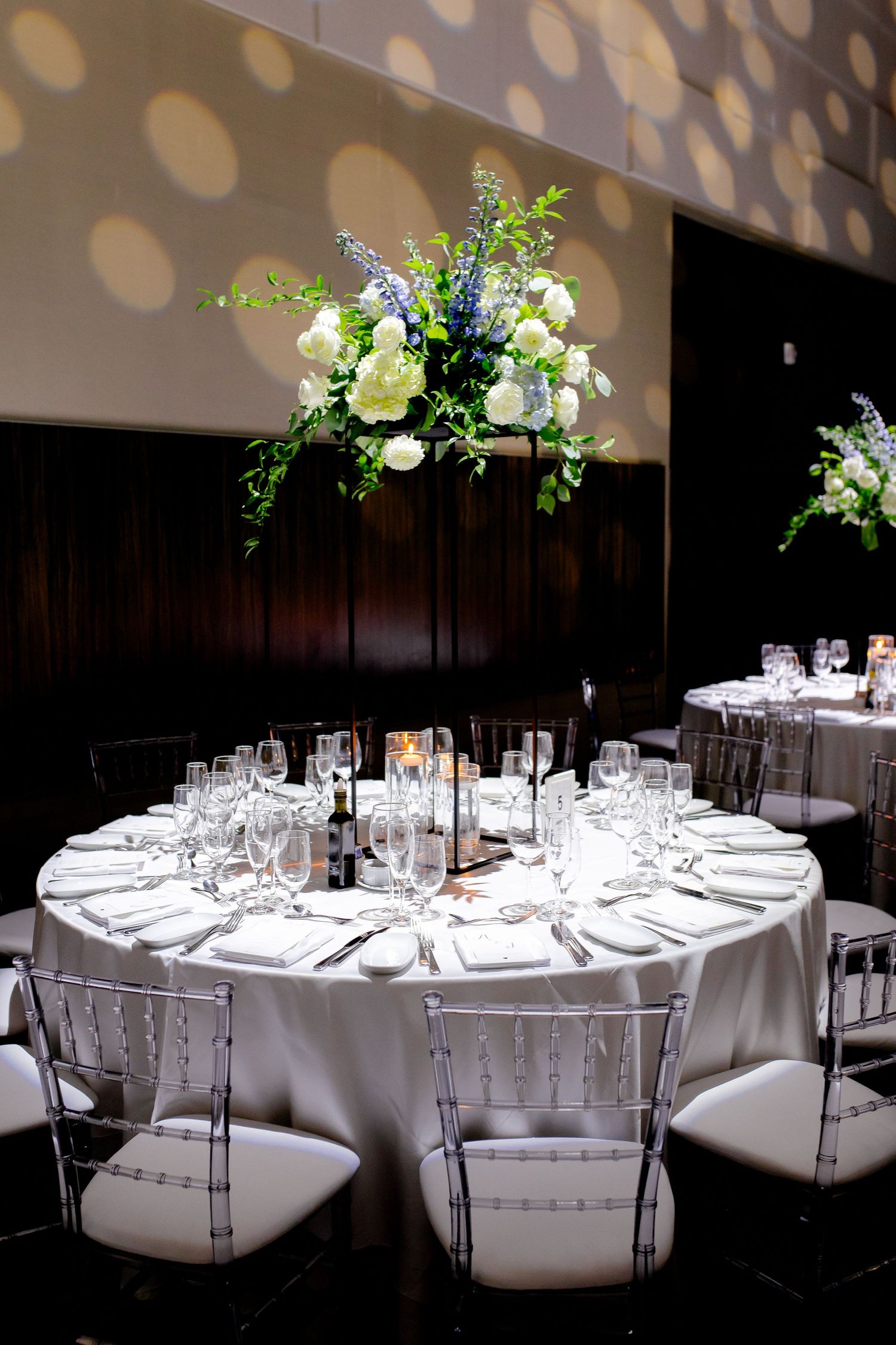 Elegant round reception table with white linens, chiavari chairs, and suspended floral centerpiece.