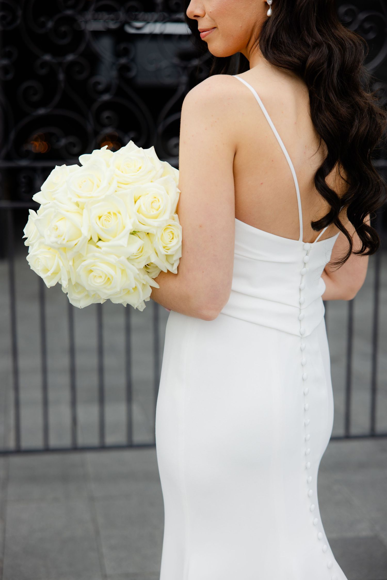 Close-up of bride's back showing elegant white dress details and cream rose bouquet.