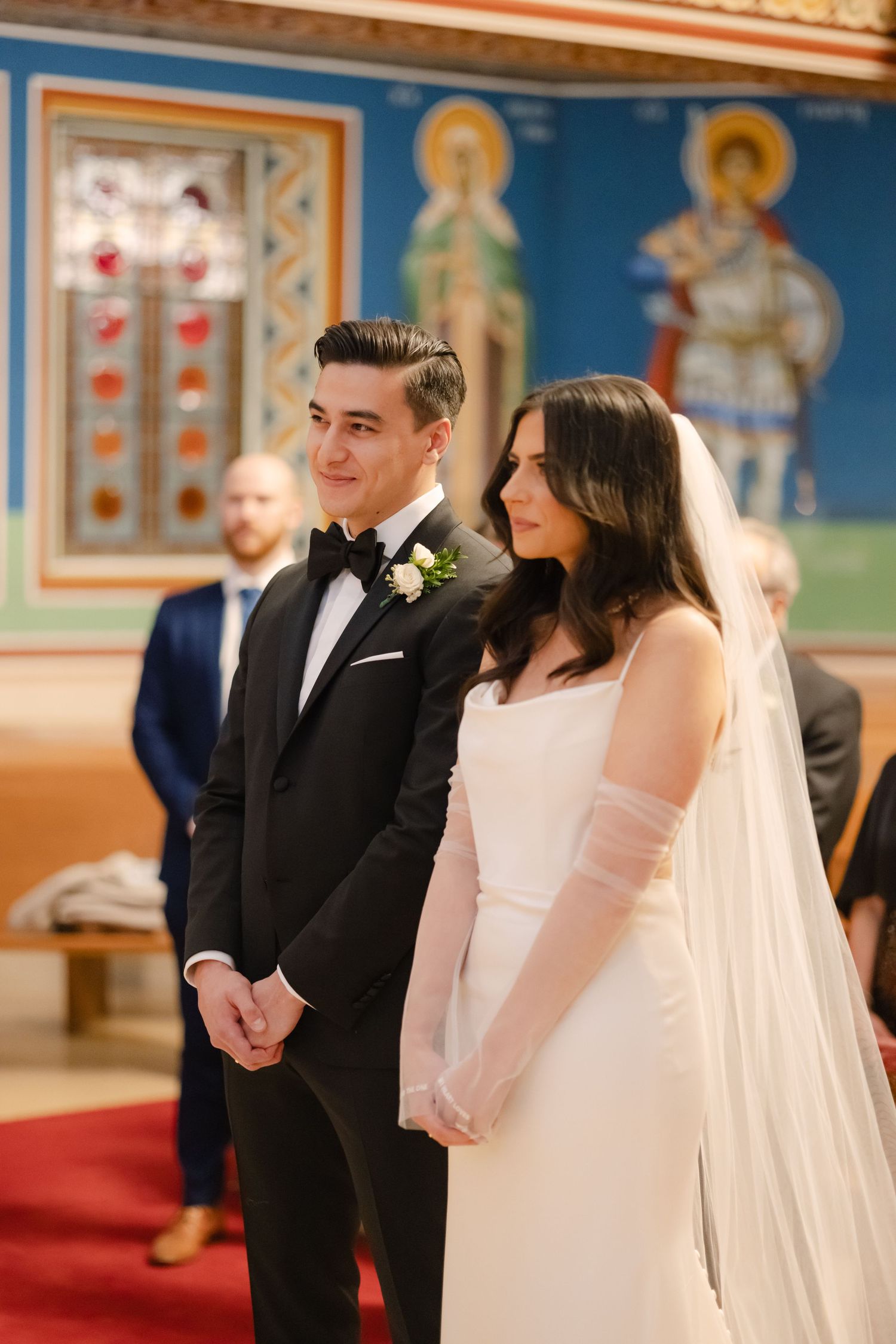 Couple at orthodox church wedding ceremony with traditional religious iconography in background.