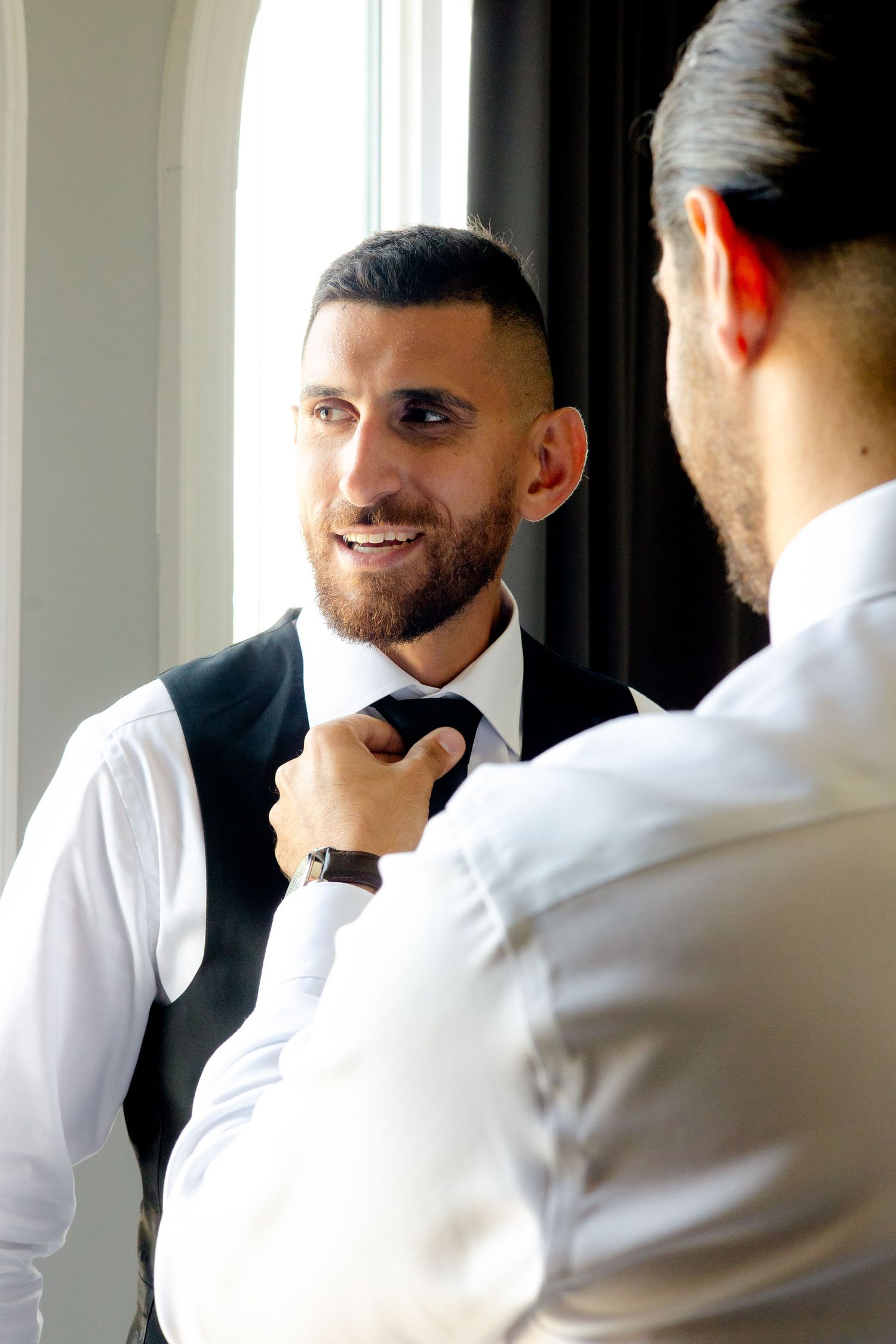 Two people in formal attire making final adjustments to a tie.