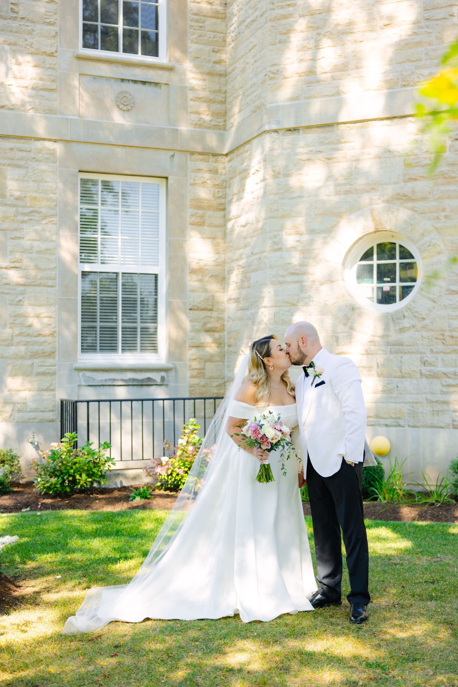 A sun-drenched wedding photo against limestone architecture with circular window detail.