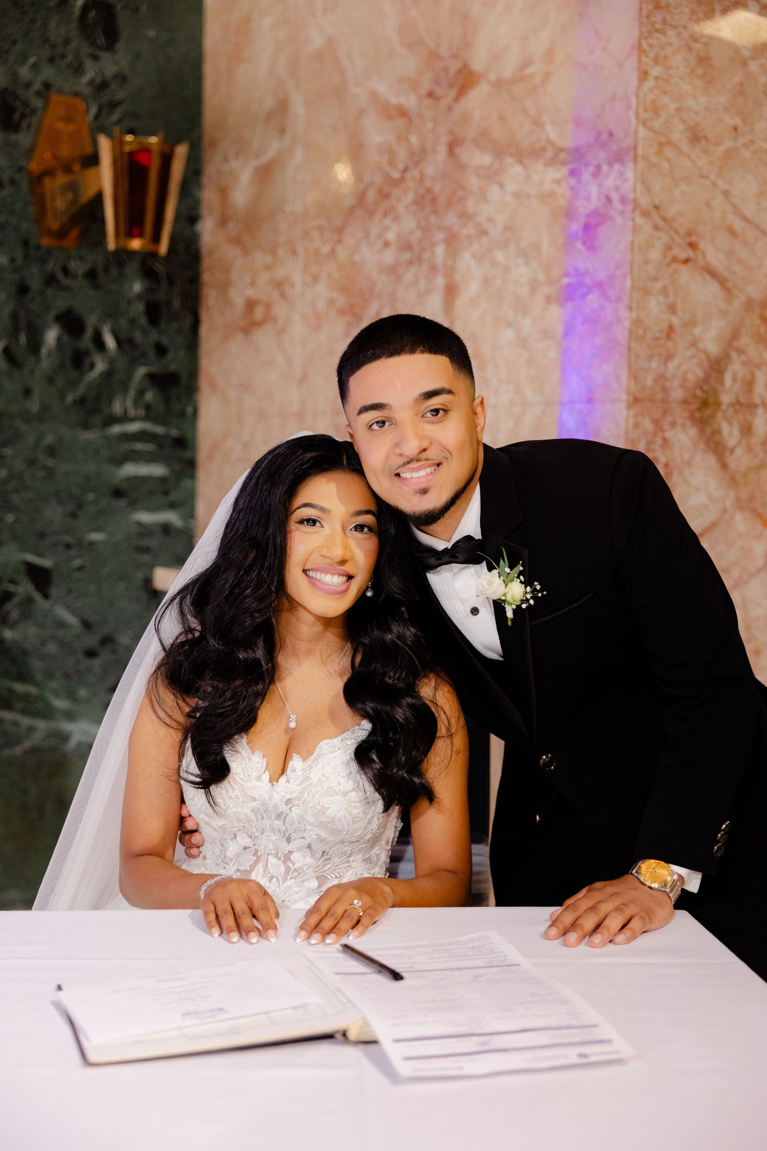 Couple signing marriage documents at white table during wedding ceremony.