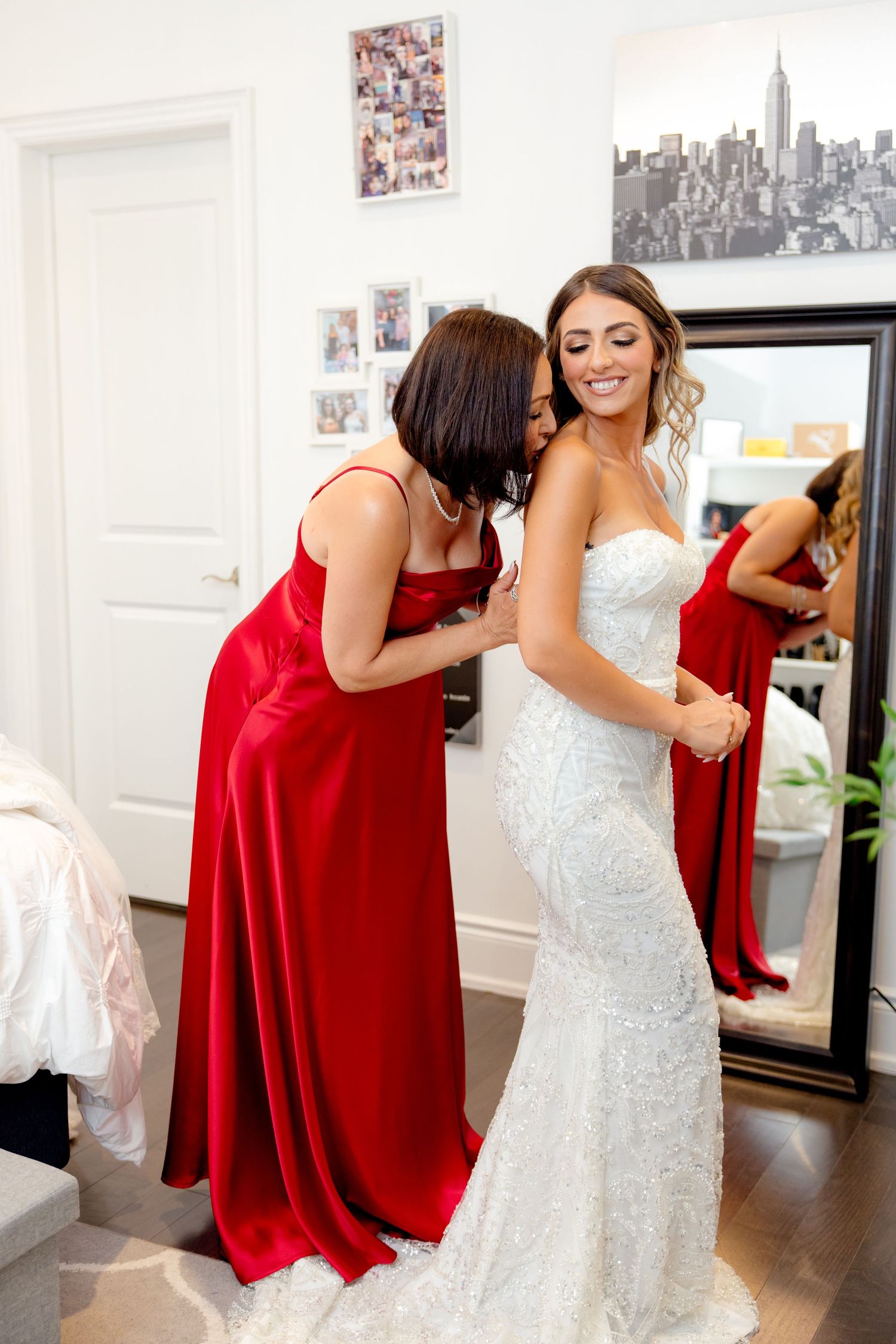 A touching moment during wedding preparations with bride in white and attendant in red gown.