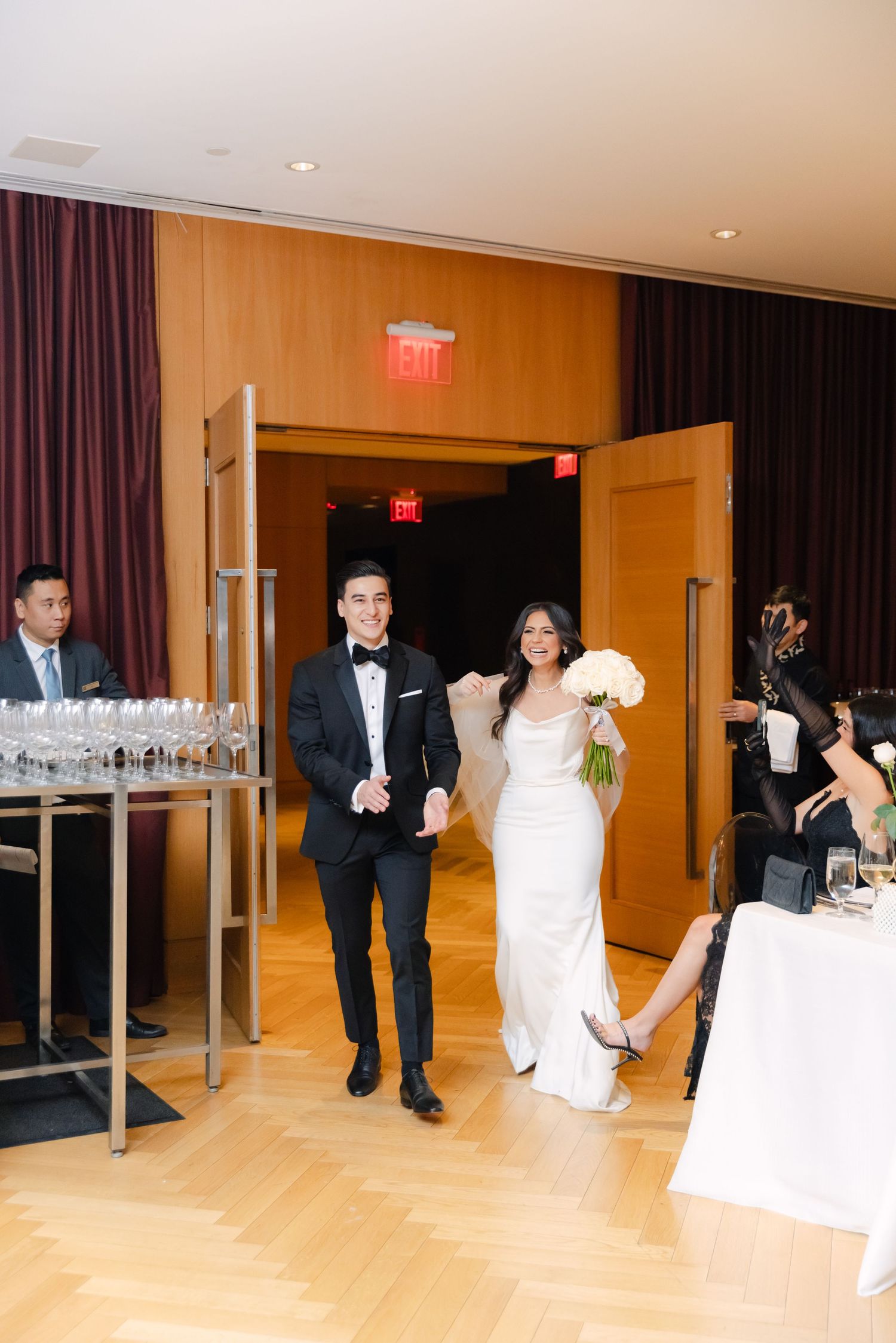 Wedding reception venue with warm wood floors and burgundy curtains at entrance.