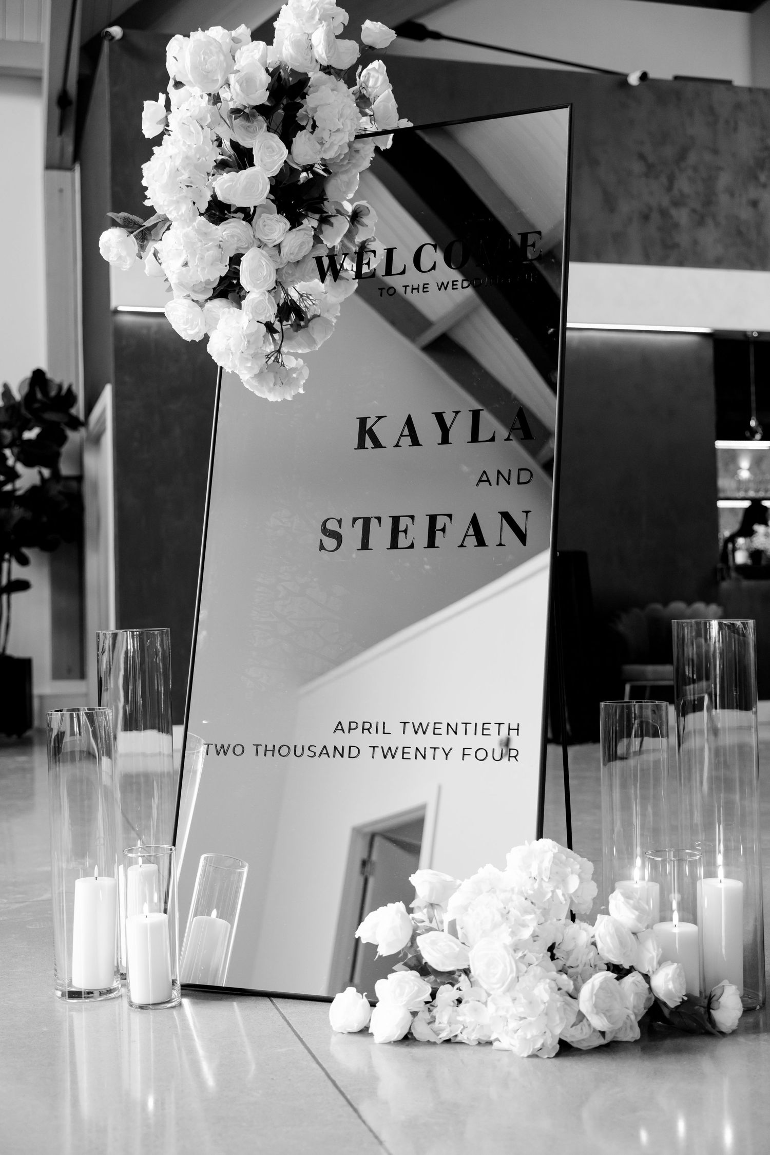 Elegant wedding welcome sign with white floral decorations and candles in black and white.