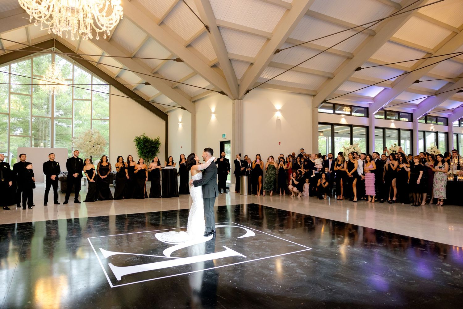 Wedding guests form circle around dance floor as couple dances under crystal chandelier.