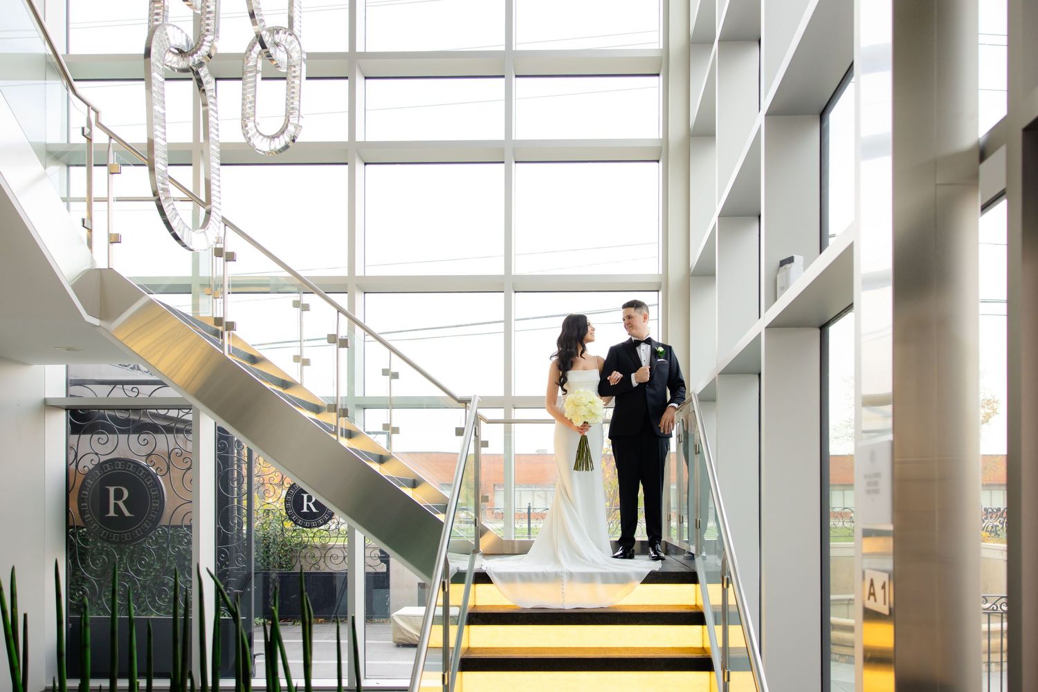 Modern architectural wedding photo with glass walls and geometric staircase design.