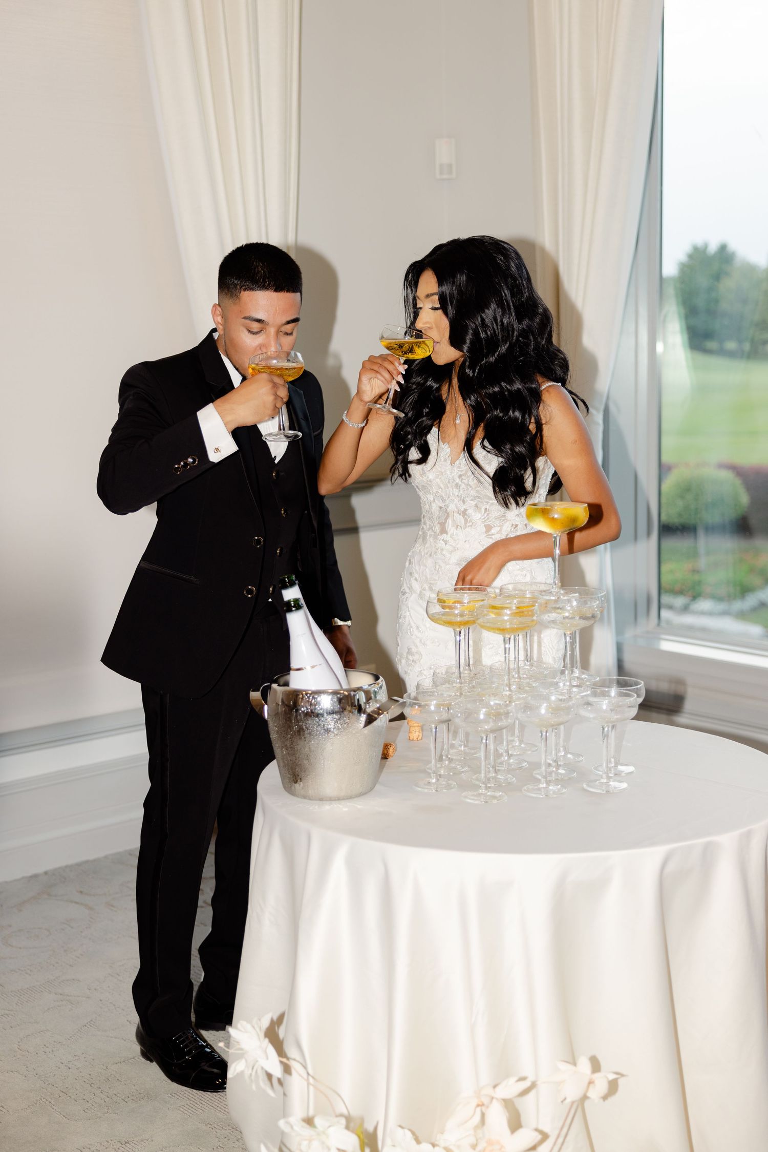 A couple sharing champagne during their wedding reception next to a tower of glasses.