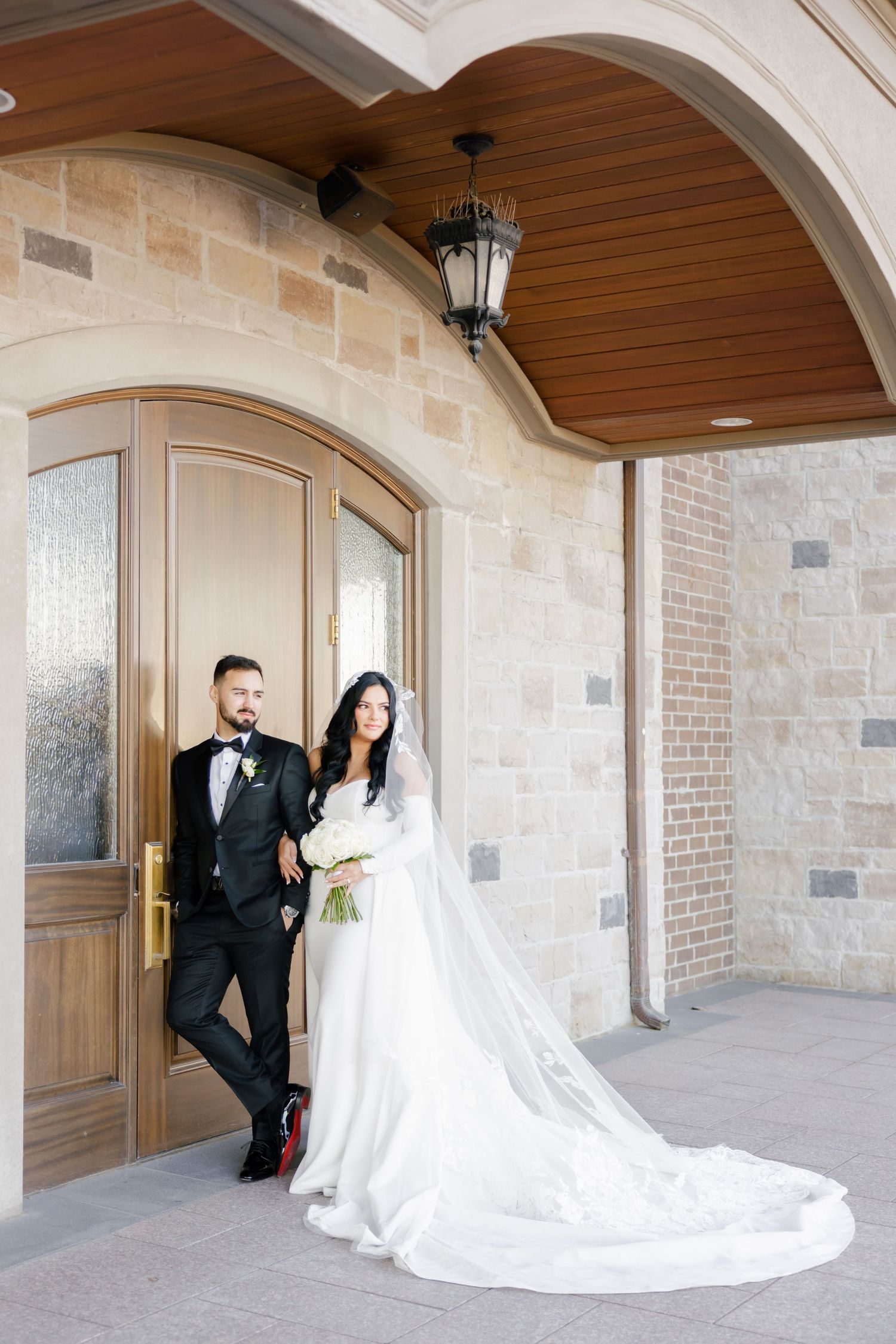 Wedding portrait under arched stone entryway with hanging lantern and wooden details.