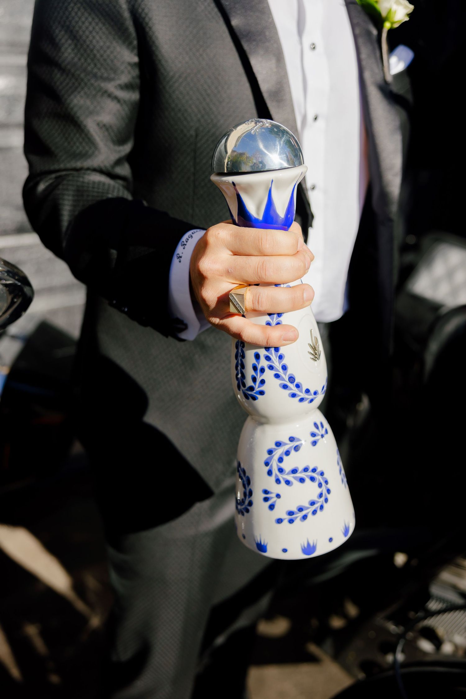 Close-up of hands holding a decorative blue and white ceramic bottle against a dark suit.