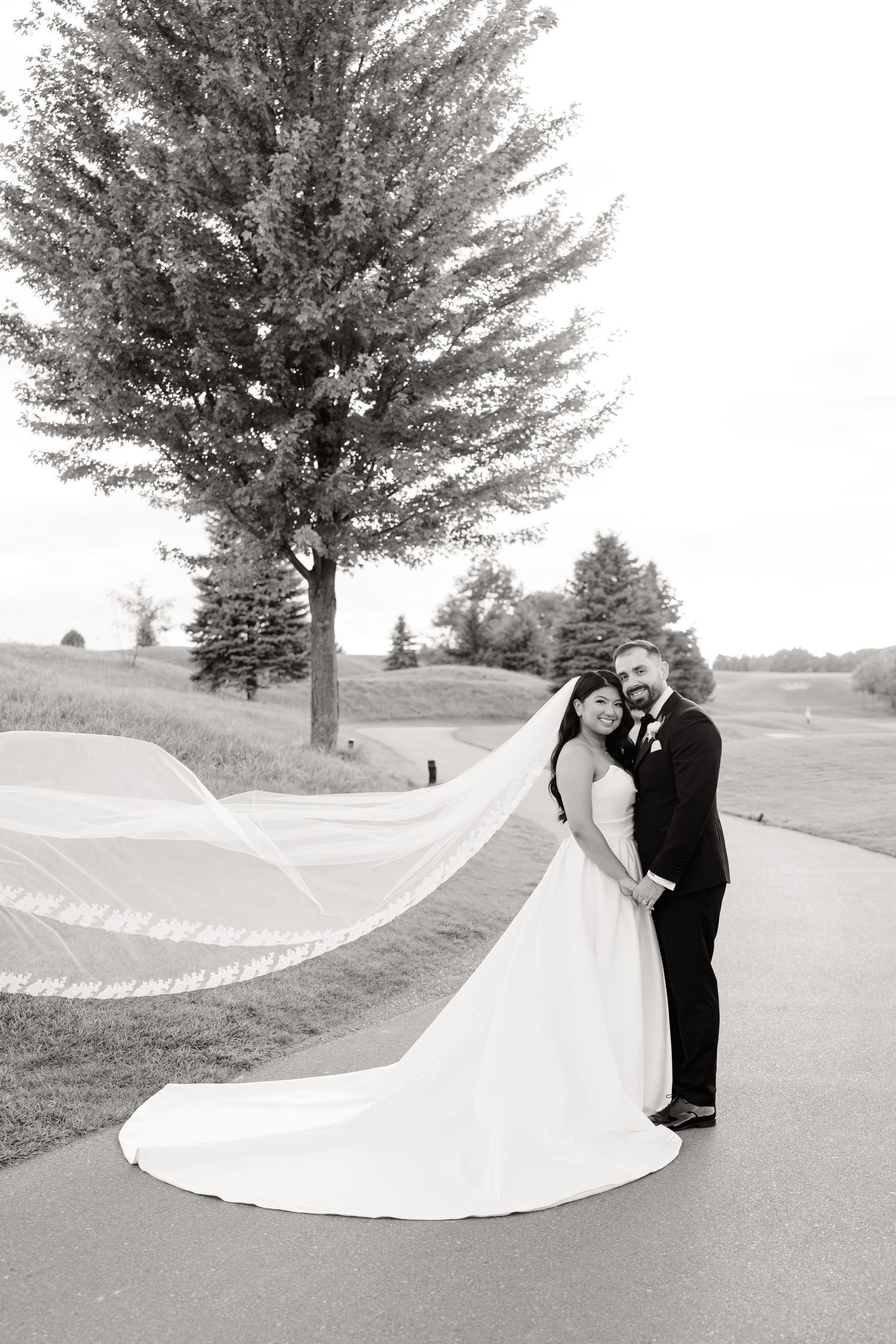 Black and white wedding portrait with flowing veil on a winding golf course path.