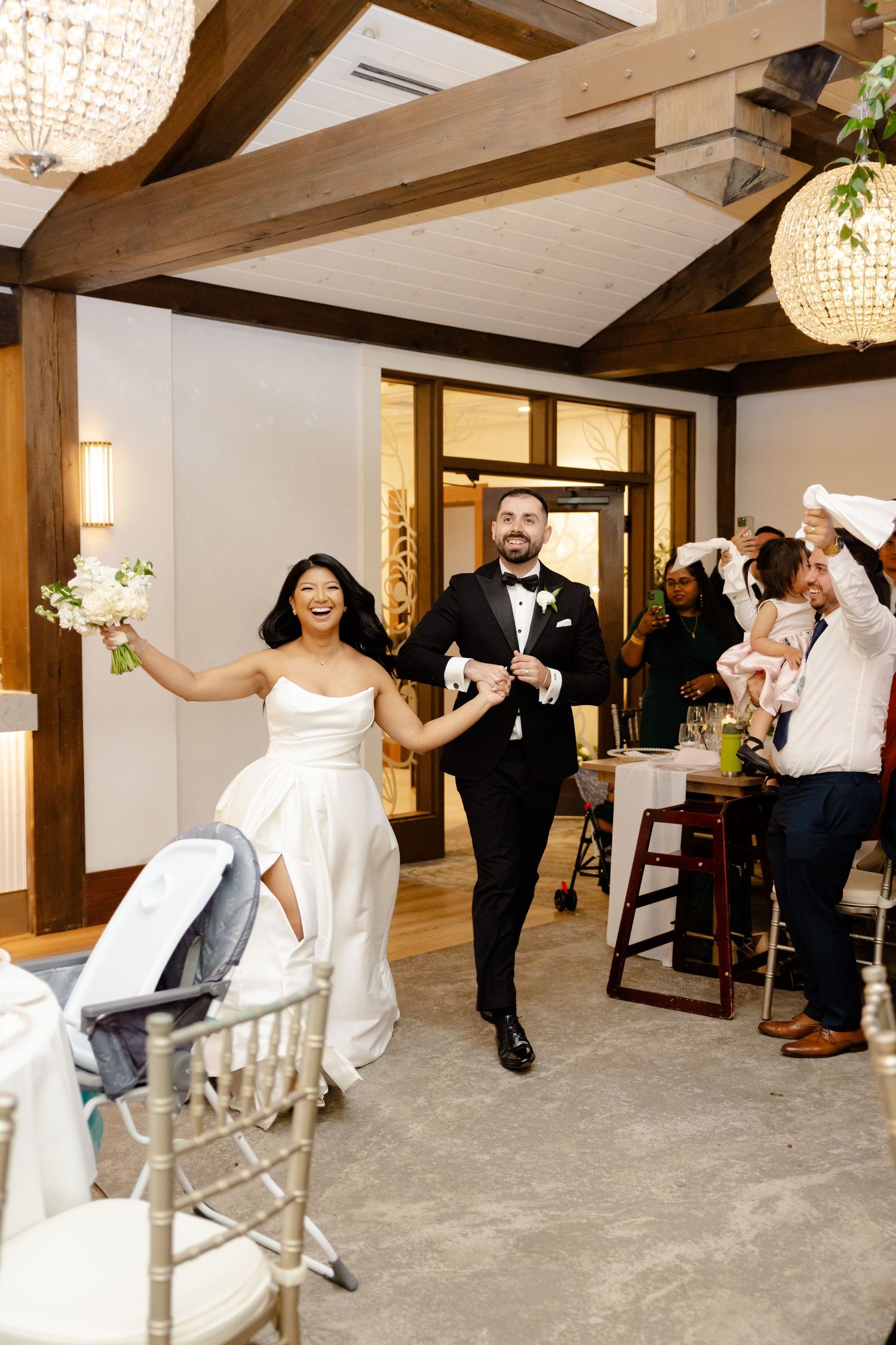 Newlyweds make their grand entrance into a rustic reception venue decorated with crystal chandeliers.