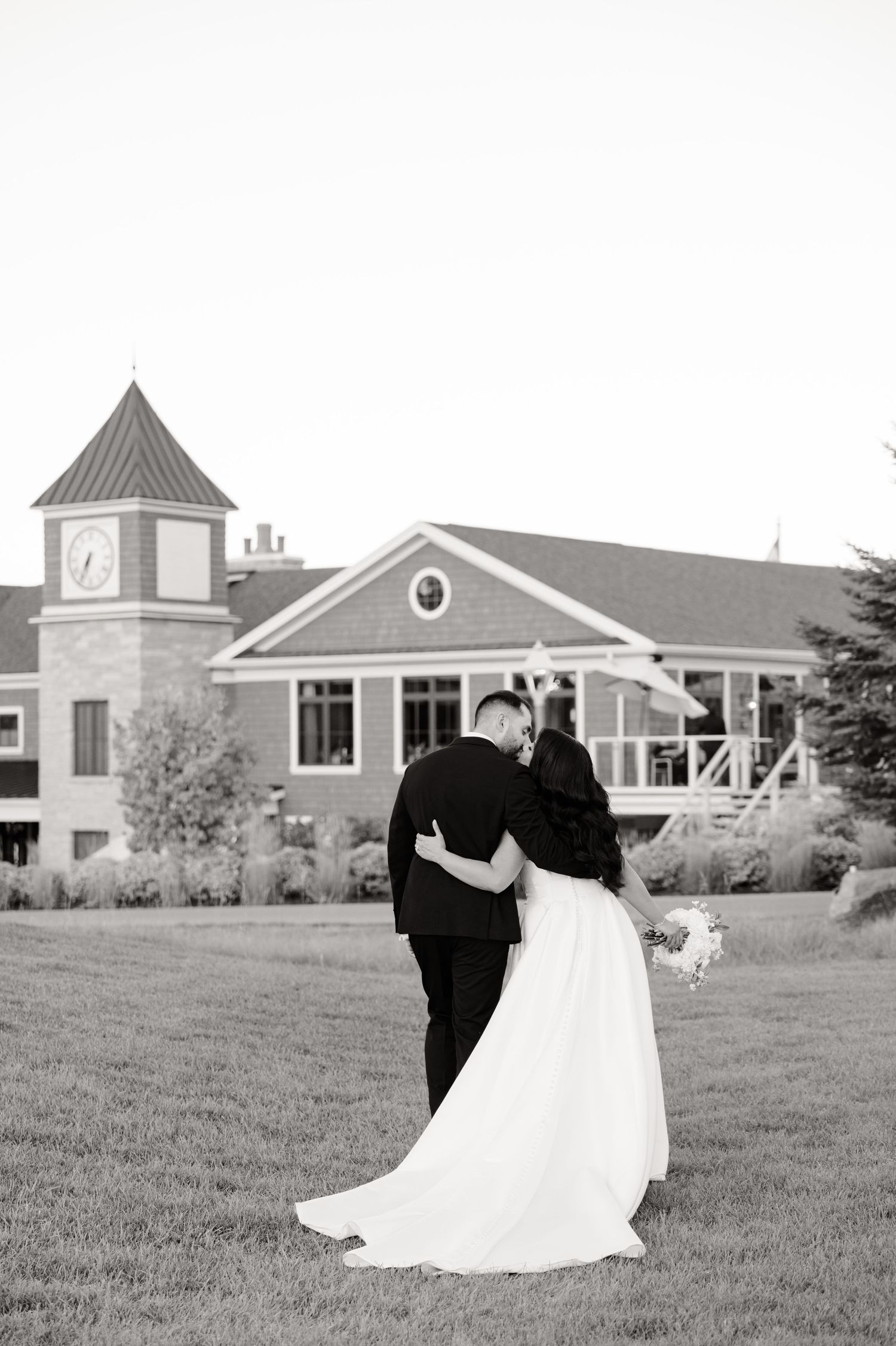 Black and white wedding photo of a couple standing before an elegant venue with a clock tower.