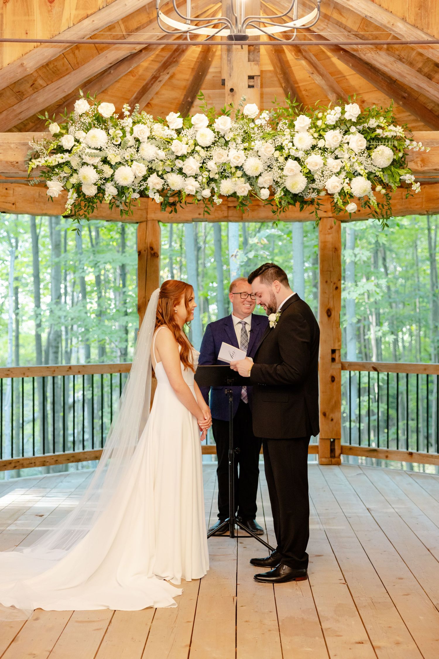 Intimate wedding ceremony moment under dramatic floral installation in woodland pavilion.