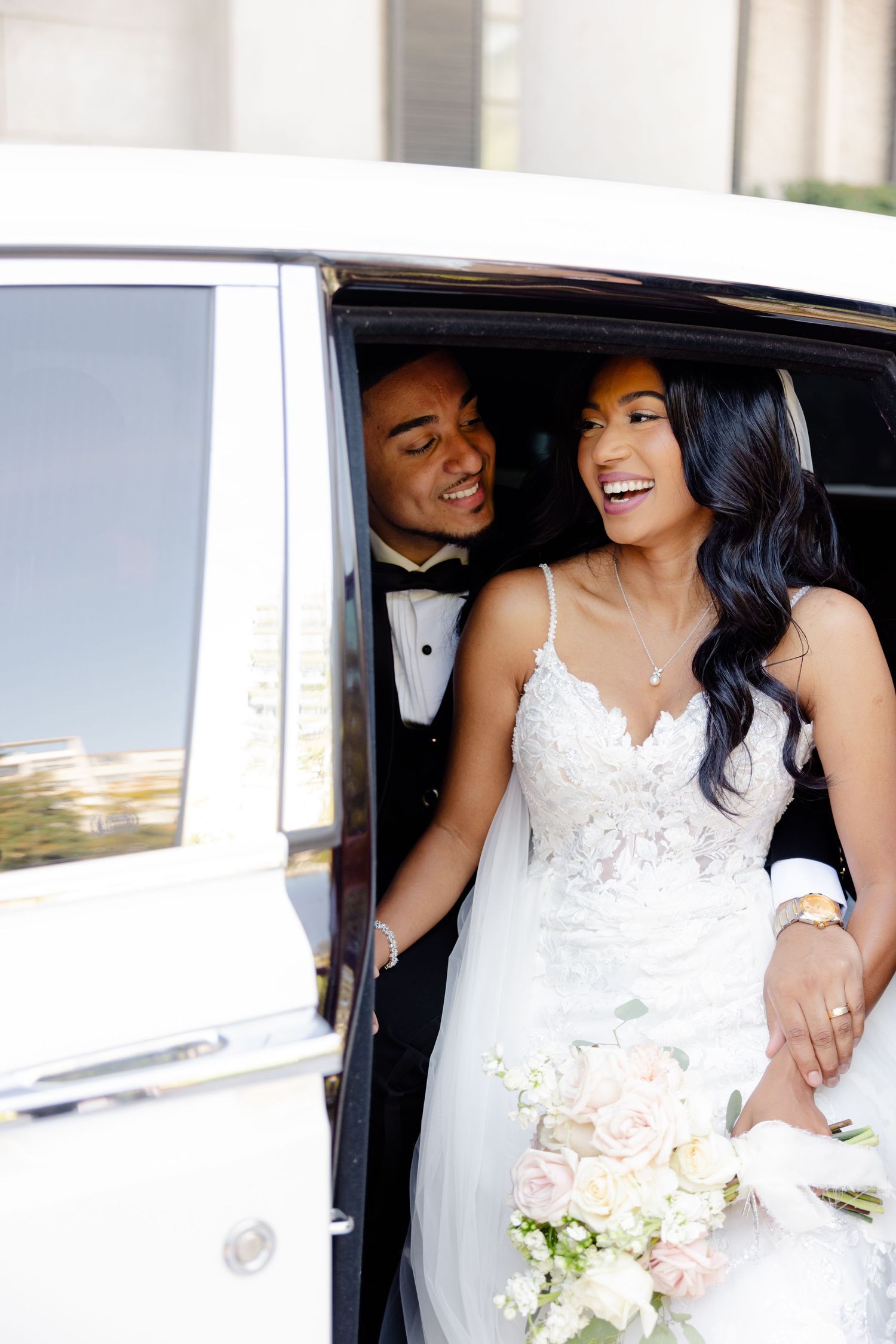 Joyful wedding couple sharing laughter in the back of a white luxury vehicle.