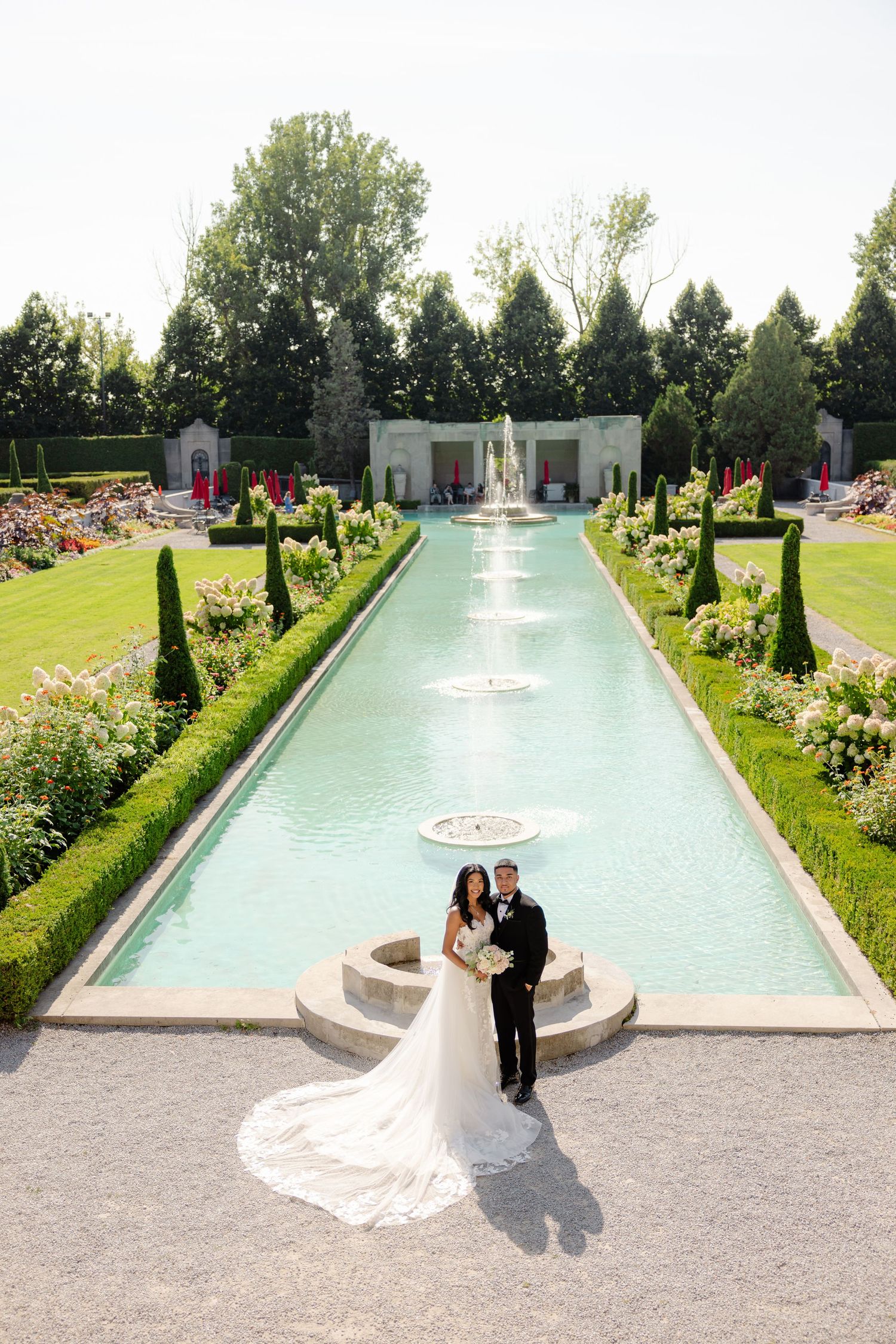 Romantic garden wedding photo with couple posed by turquoise reflecting pool and fountains.