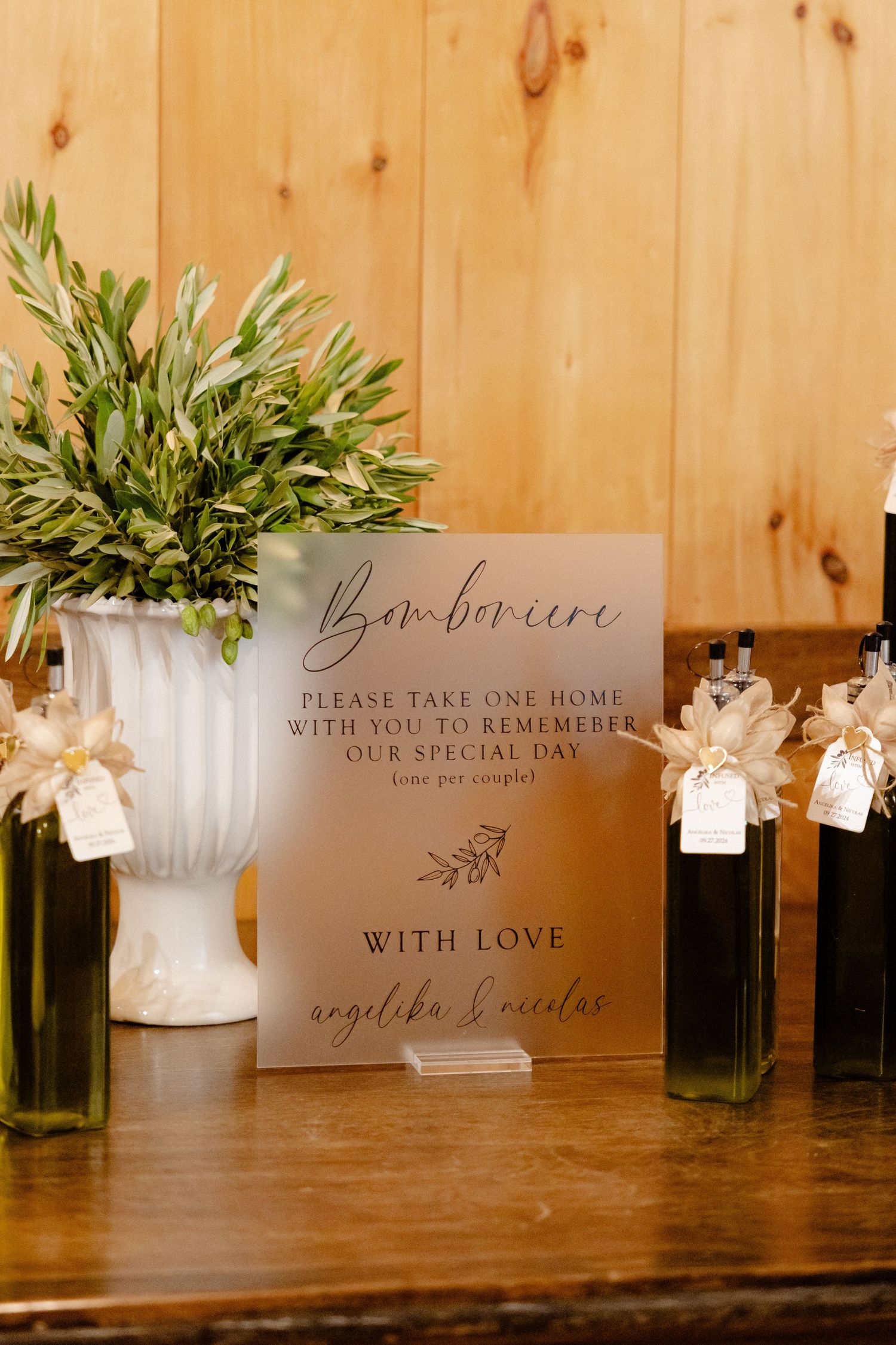 A wedding favor sign for Bon-bons displayed with decorated olive oil bottles and greenery.