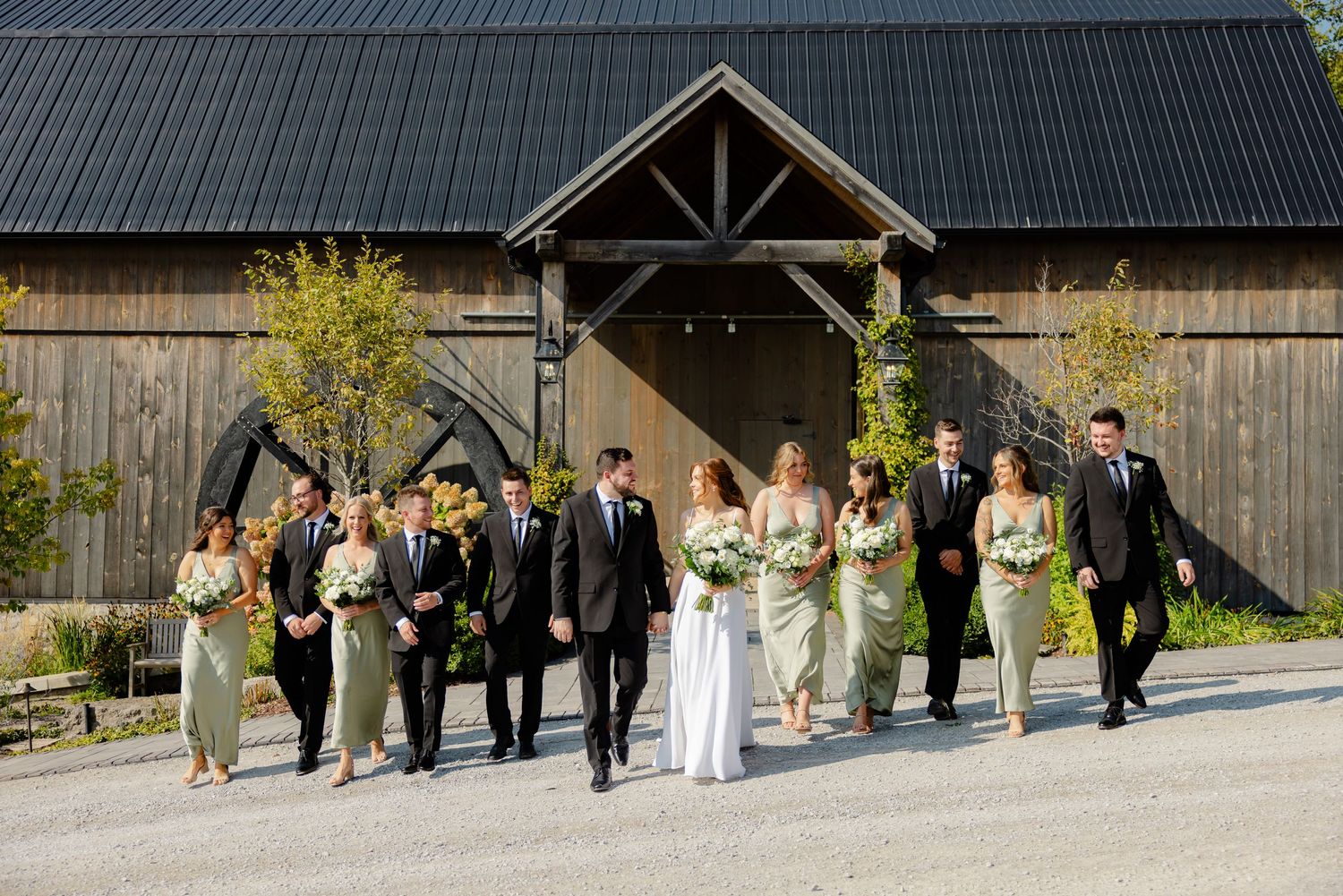Candid shot of wedding party walking along gravel path in front of rustic barn venue.