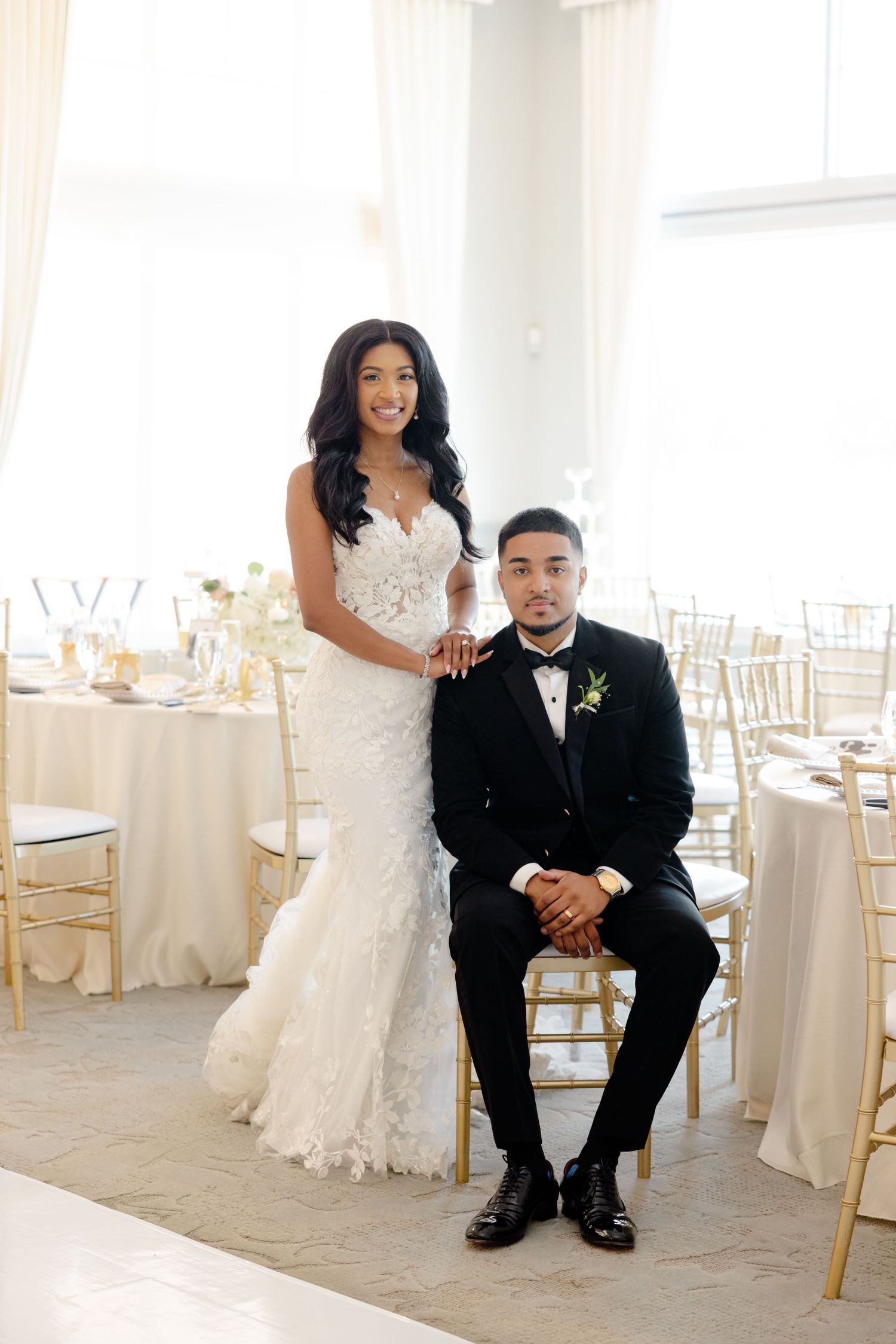 Elegant wedding portrait in bright reception hall with gold chiavari chairs and white decor.