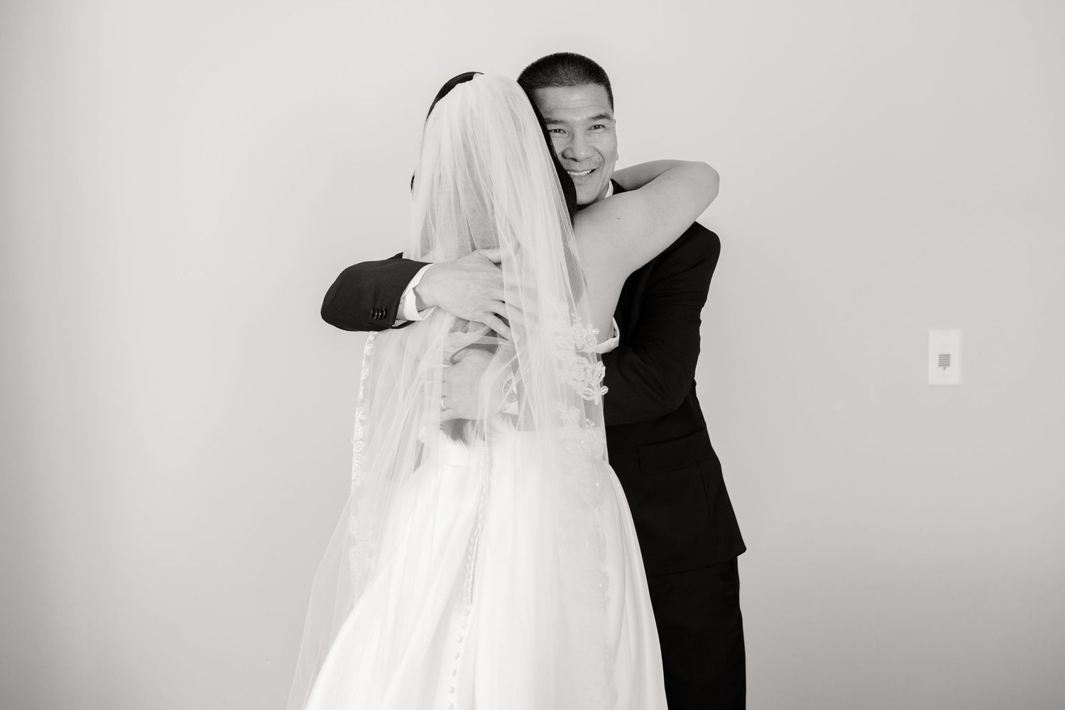 Black and white candid photo of newlyweds embracing during intimate wedding moment.