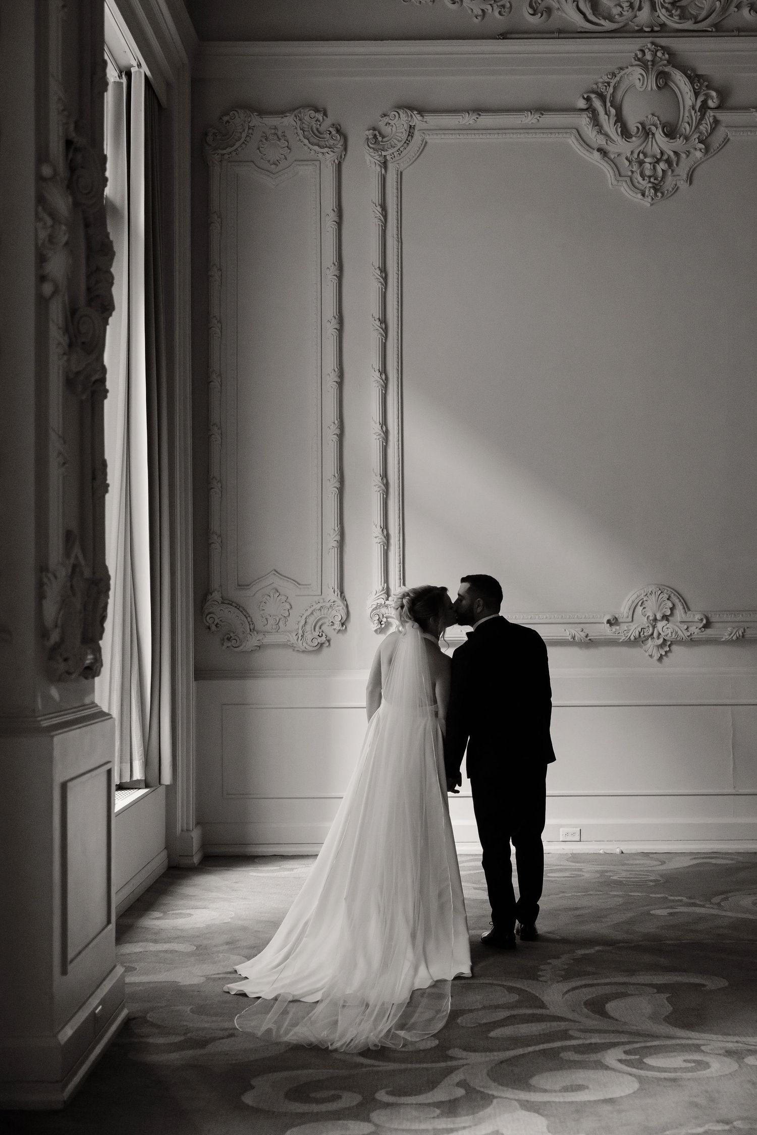 Moody black and white wedding portraits captured in a historic room with decorative moldings.