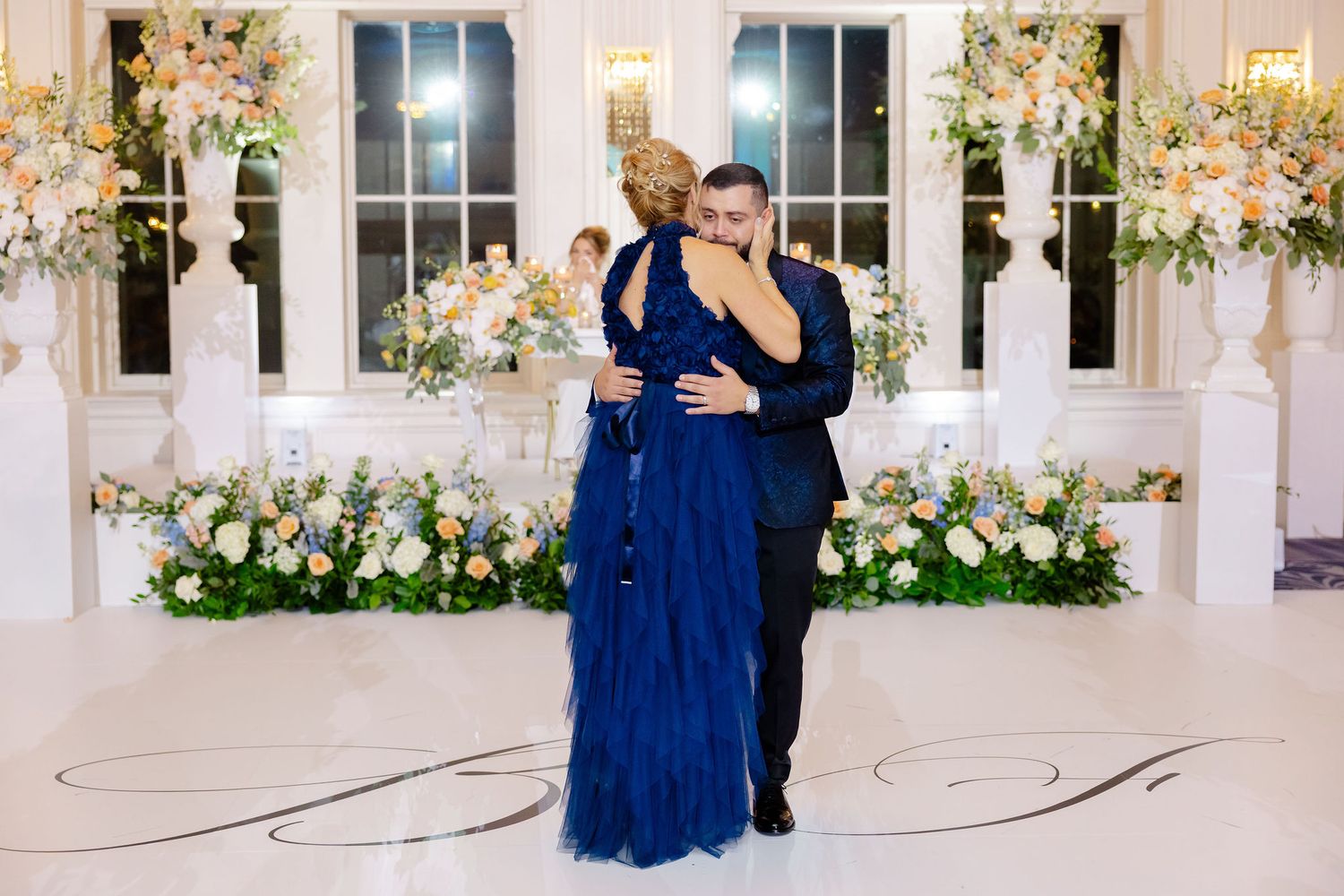 Wedding party members in navy blue attire dancing during reception in an elegant white ballroom.