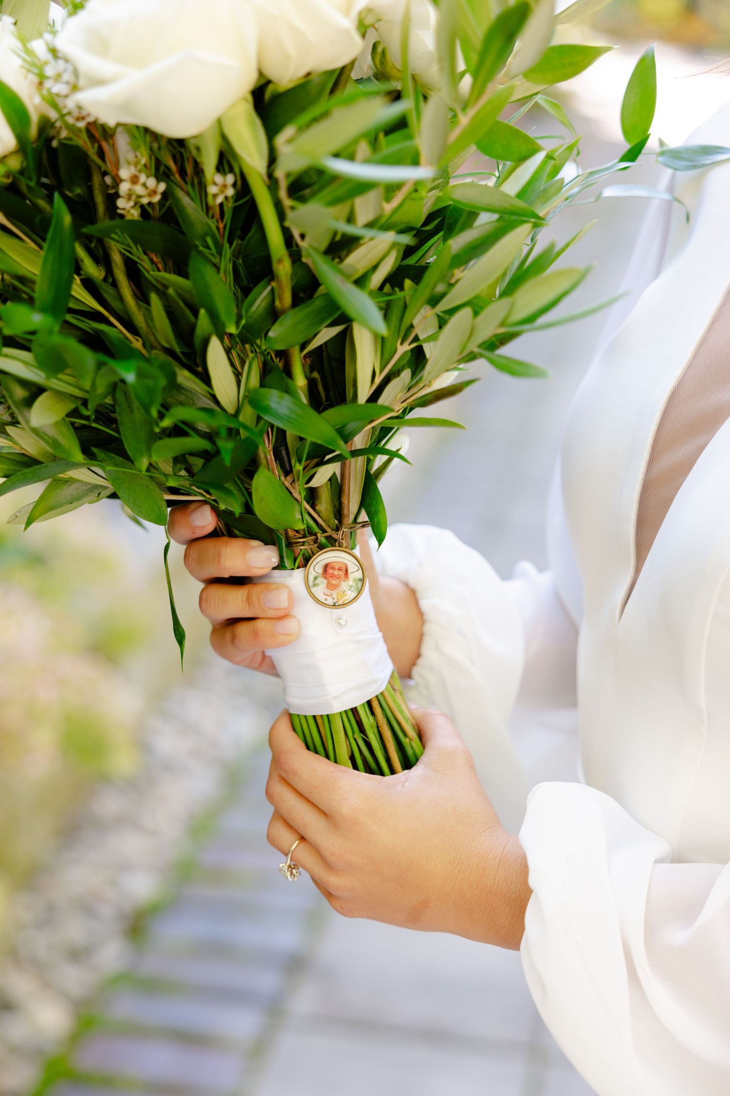 Detail shot of hands holding white rose bouquet wrapped with silk ribbon.