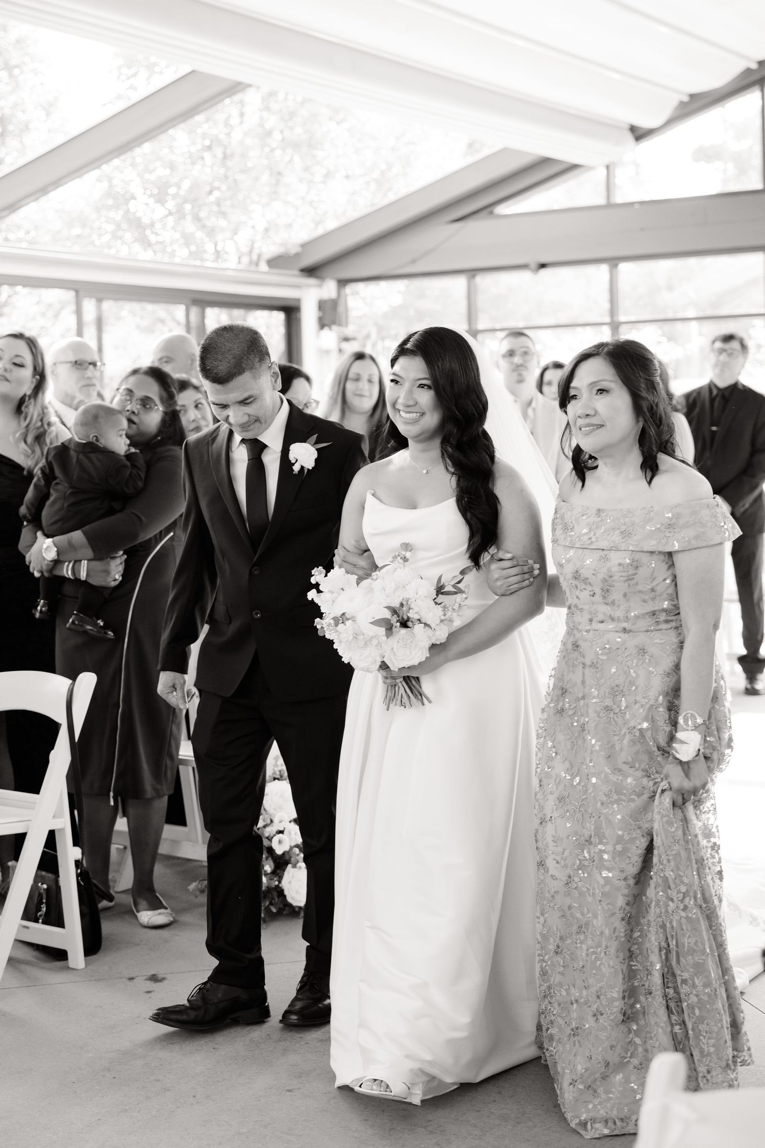 Black and white photo of a wedding processional in a sleek modern venue with natural lighting.