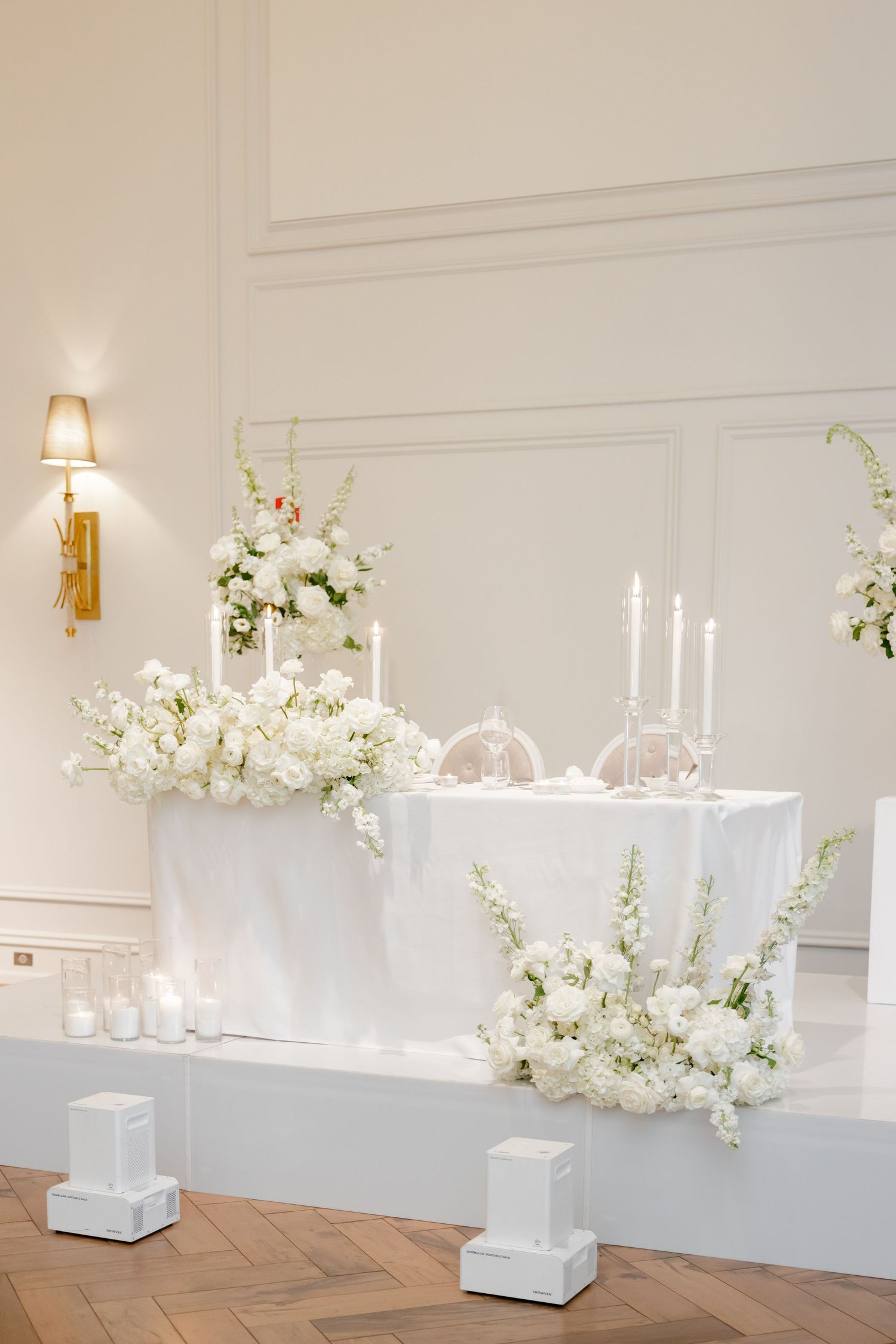 White wedding head table with taper candles and cascading floral arrangements on raised platform.