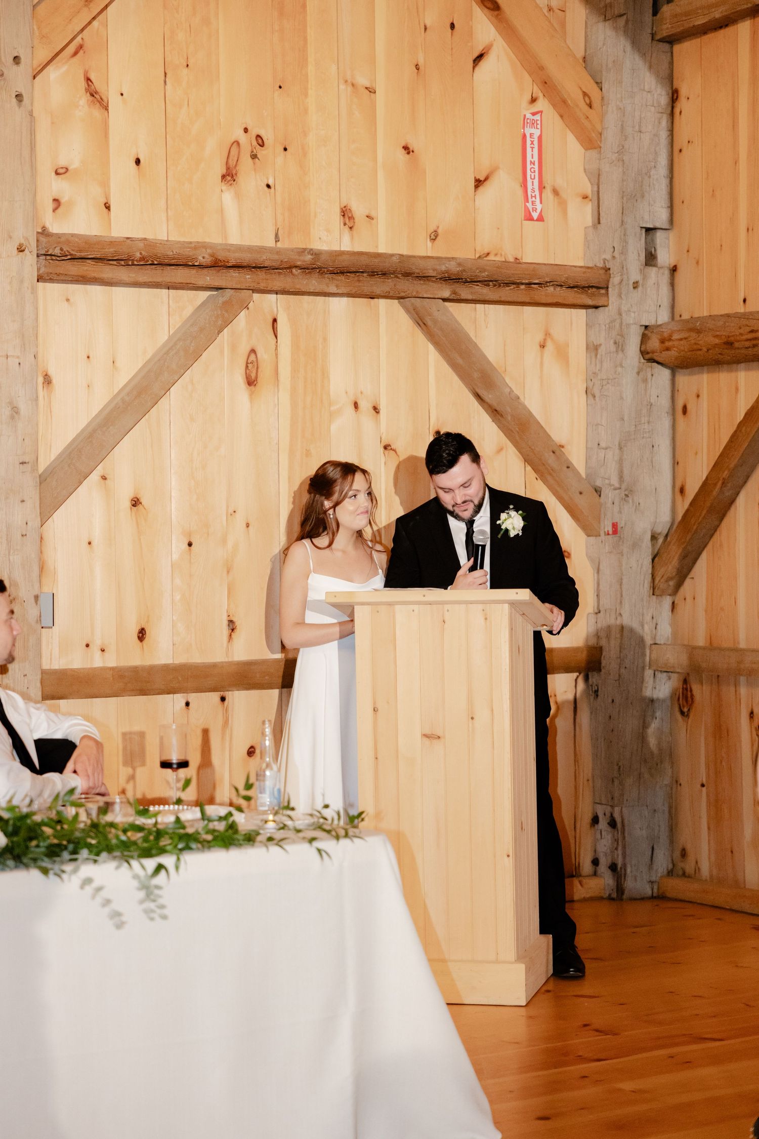 A couple stands at a wooden podium during their wedding ceremony in a rustic barn setting.