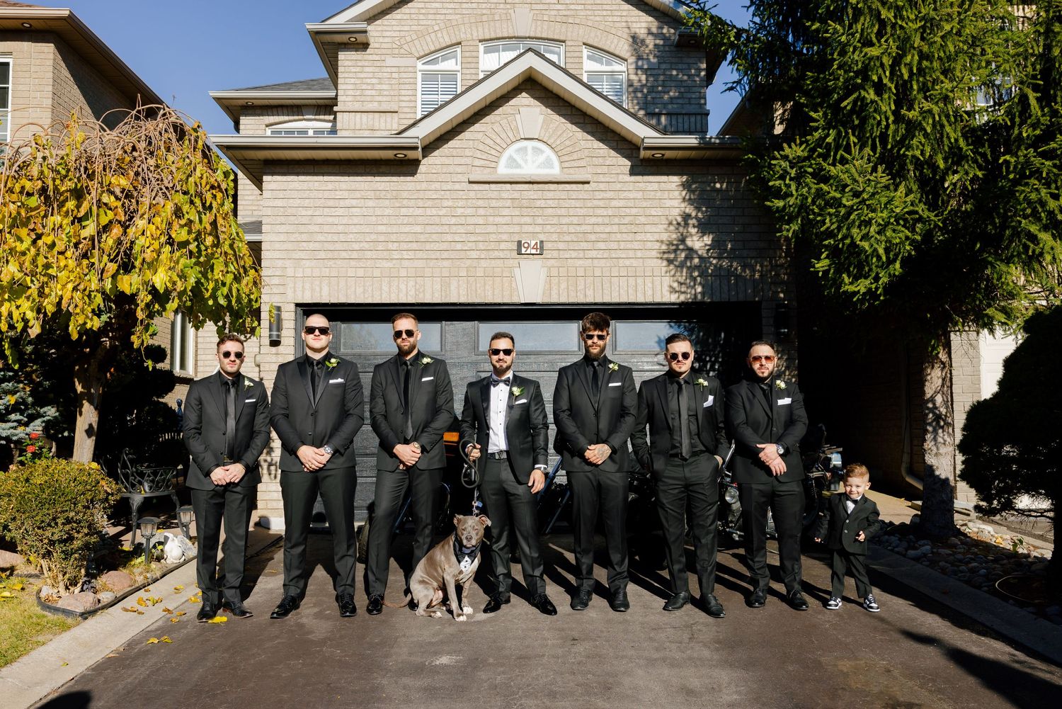 A formal group photo with a dog in front of a suburban house.