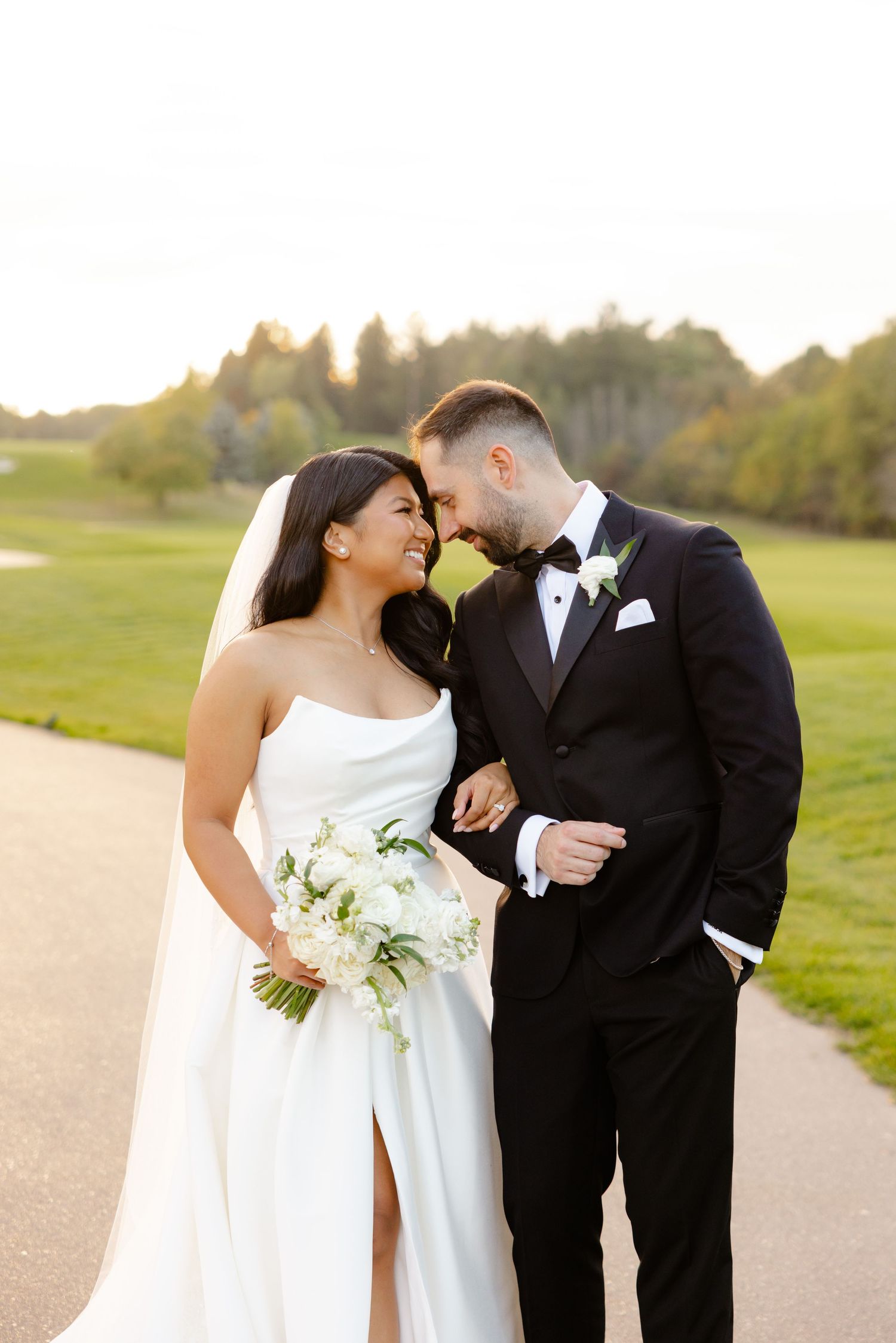 A romantic wedding portrait of a couple on a golf course path with the bride holding a white bouquet.