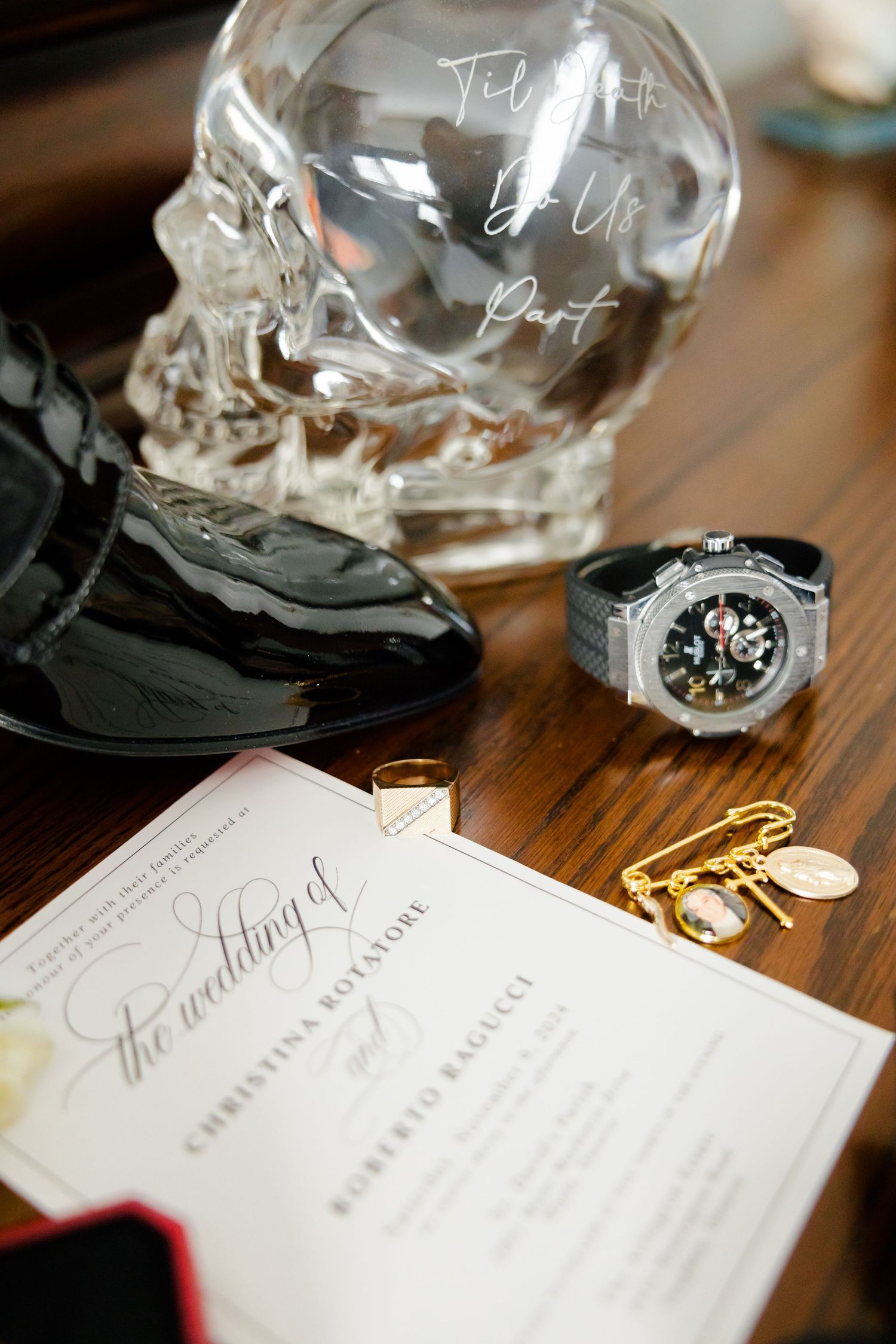 Crystal skull decanter with watch, invitation and accessories on wooden surface.