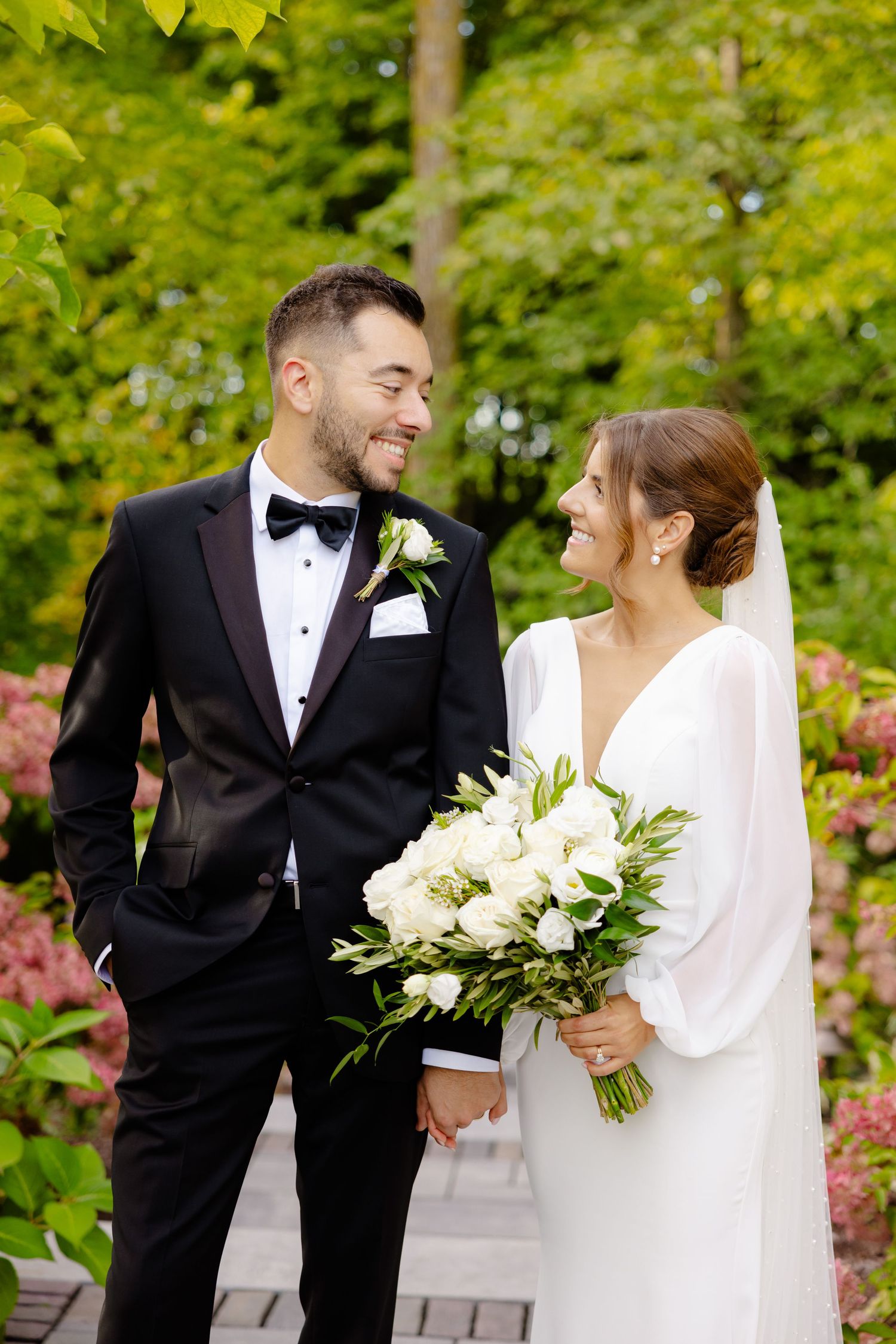 Candid wedding moment captured with couple sharing smiles amidst garden greenery.