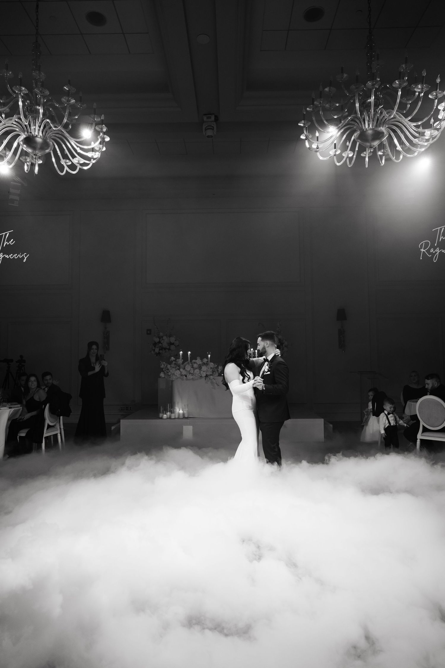Black and white photo of a wedding couple's first dance amidst dramatic fog and chandelier lighting.