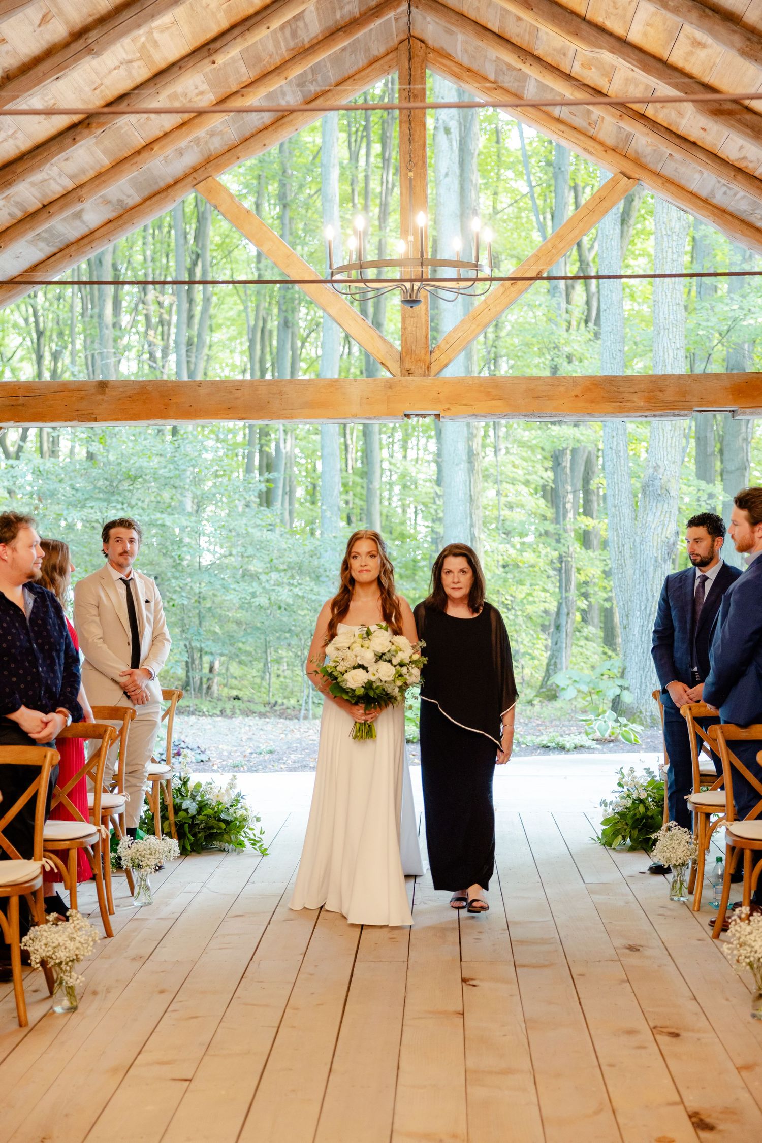 Wedding ceremony view showing decorated aisle in rustic wooden pavilion with forest backdrop.