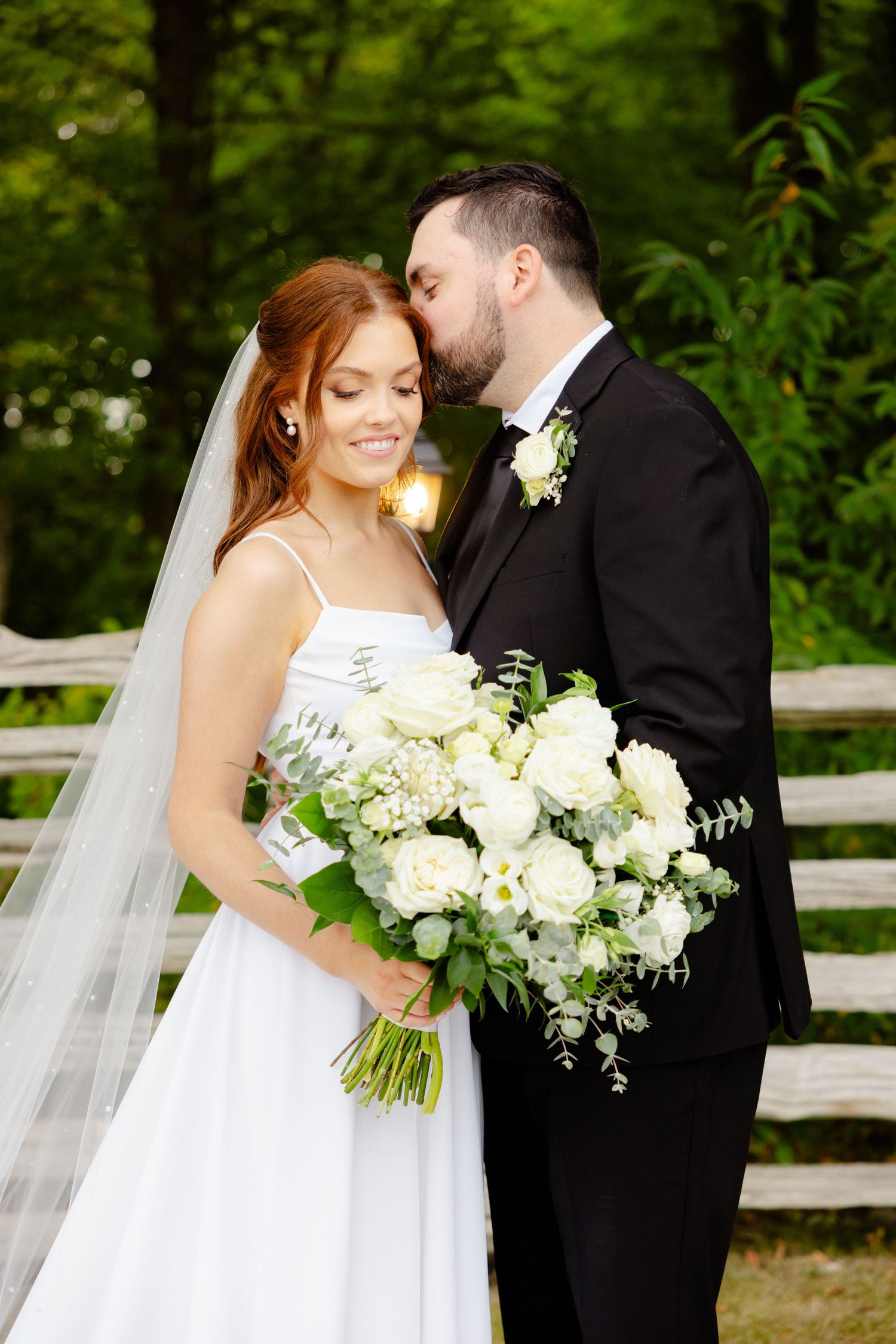 Intimate wedding moment captured with bride holding white bouquet against forest backdrop.