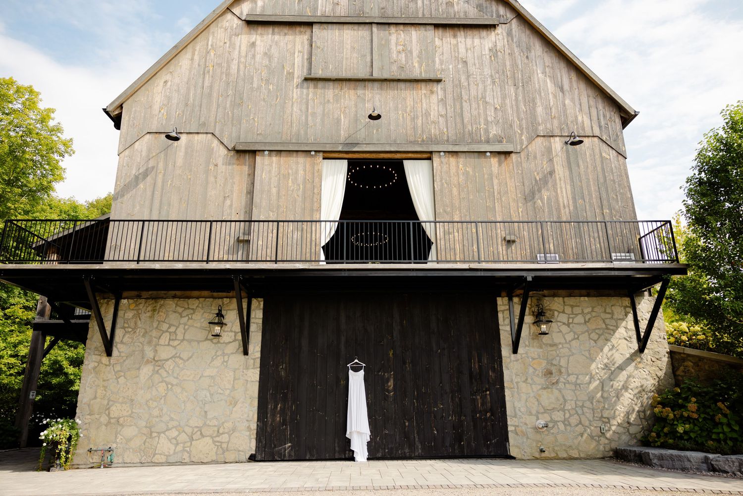 A rustic barn wedding venue with white concrete base and weathered wood siding features dramatic black double doors.