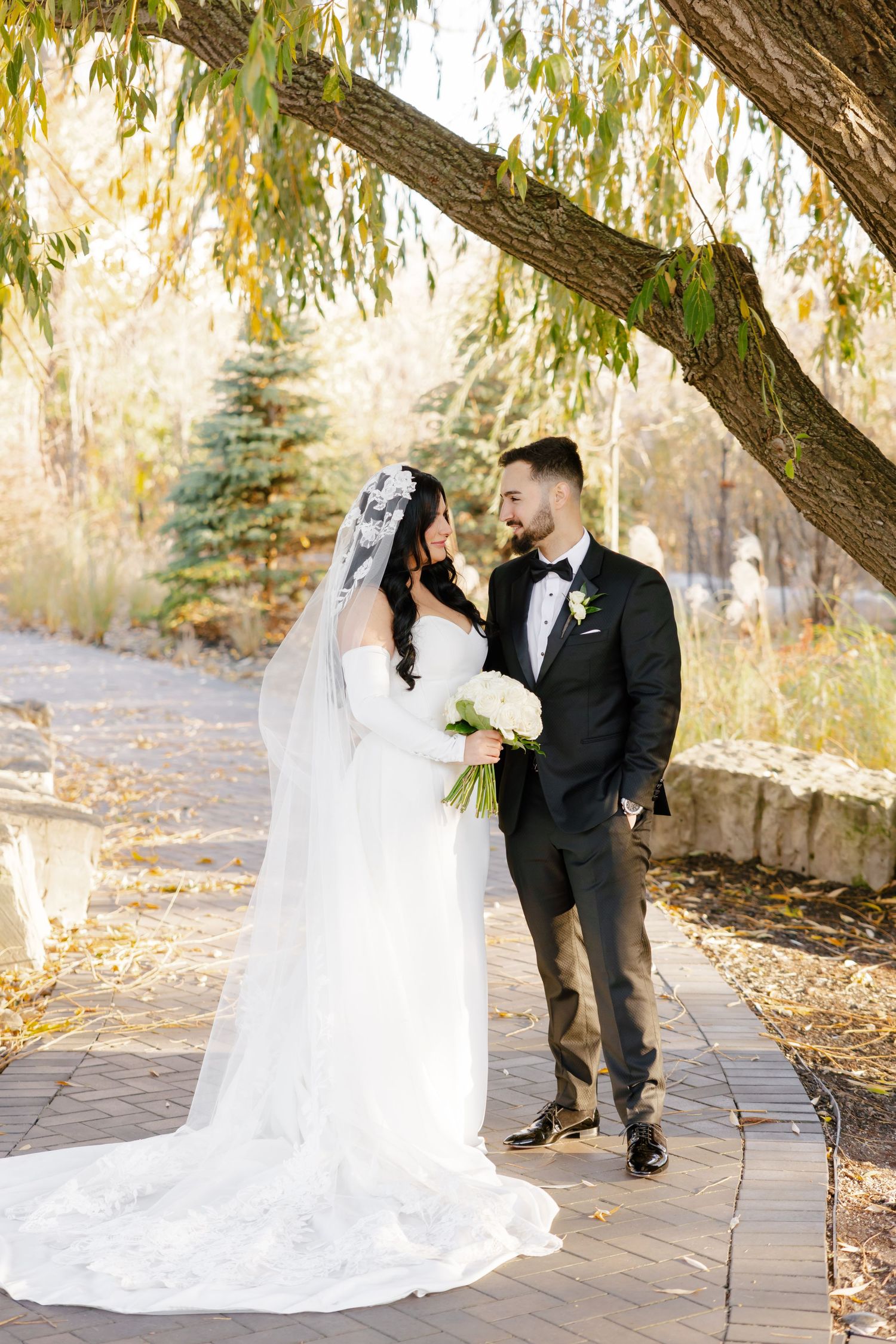 A romantic wedding portrait under a willow tree with autumn foliage.
