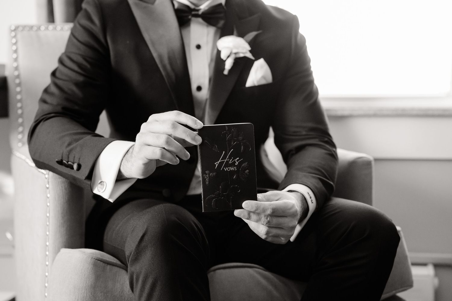 Black and white image of someone in formal attire holding a small box while seated.